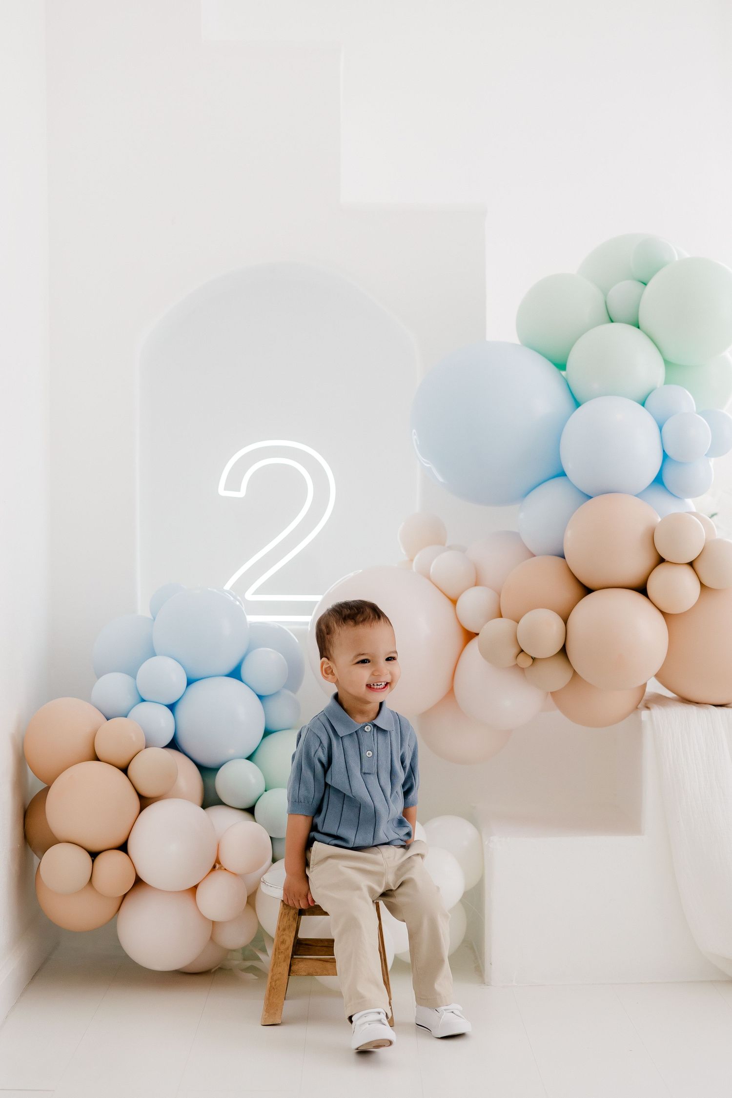 Minimalist photo studio setup with pastel balloon garland in peach and blue against white wall.