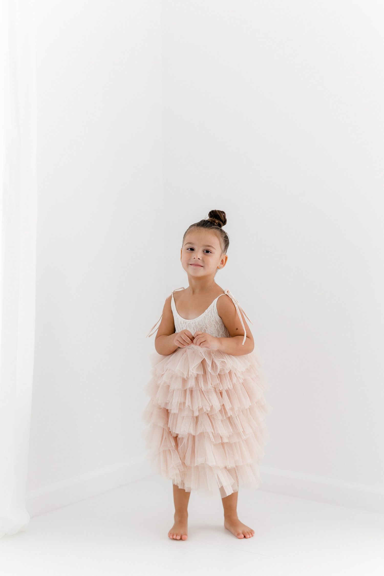 Young dancer in layered pink tulle dress stands poised against white background.