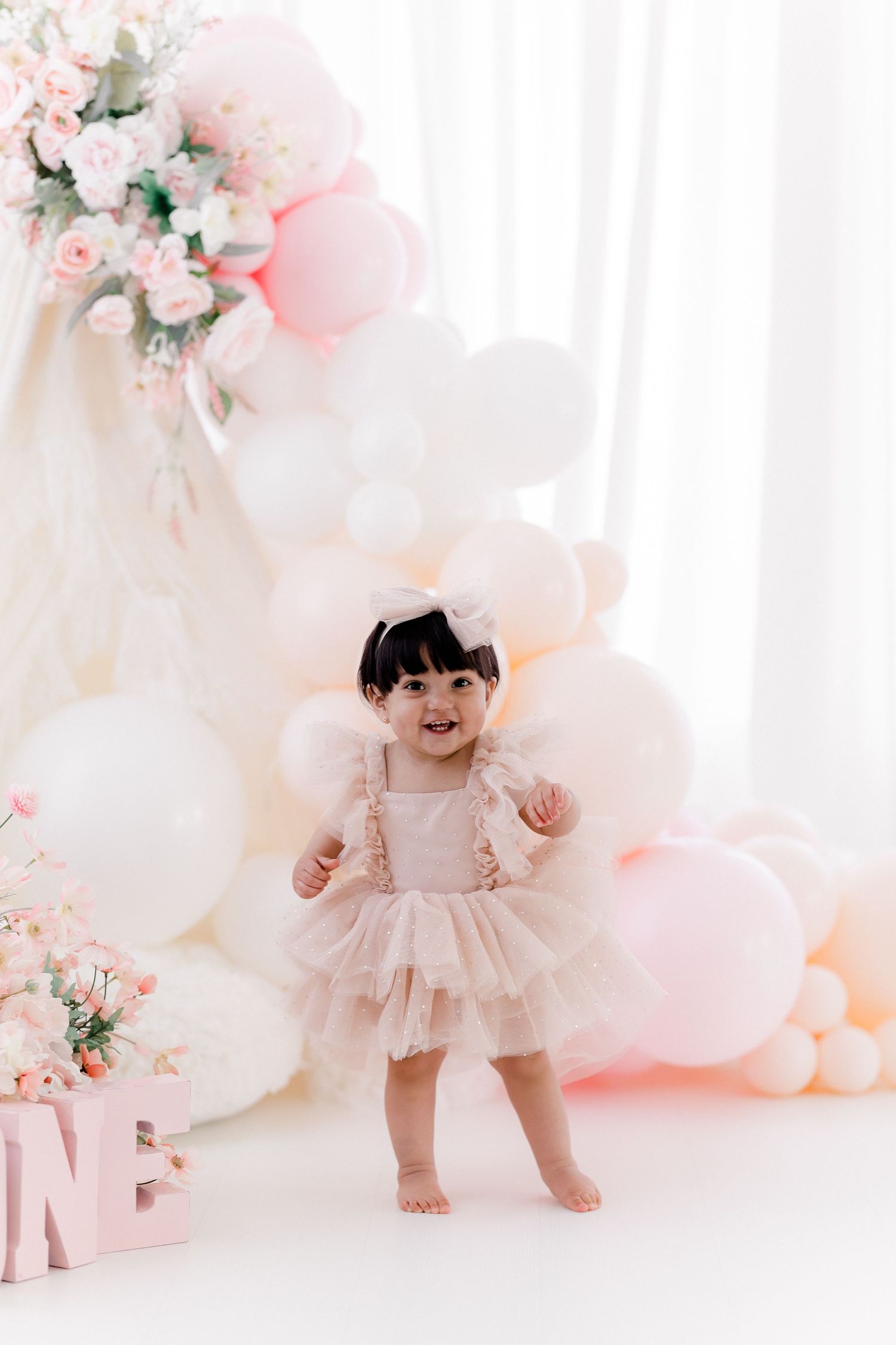 Dreamy pink and white balloon backdrop with floral arrangements for special occasion photoshoot.