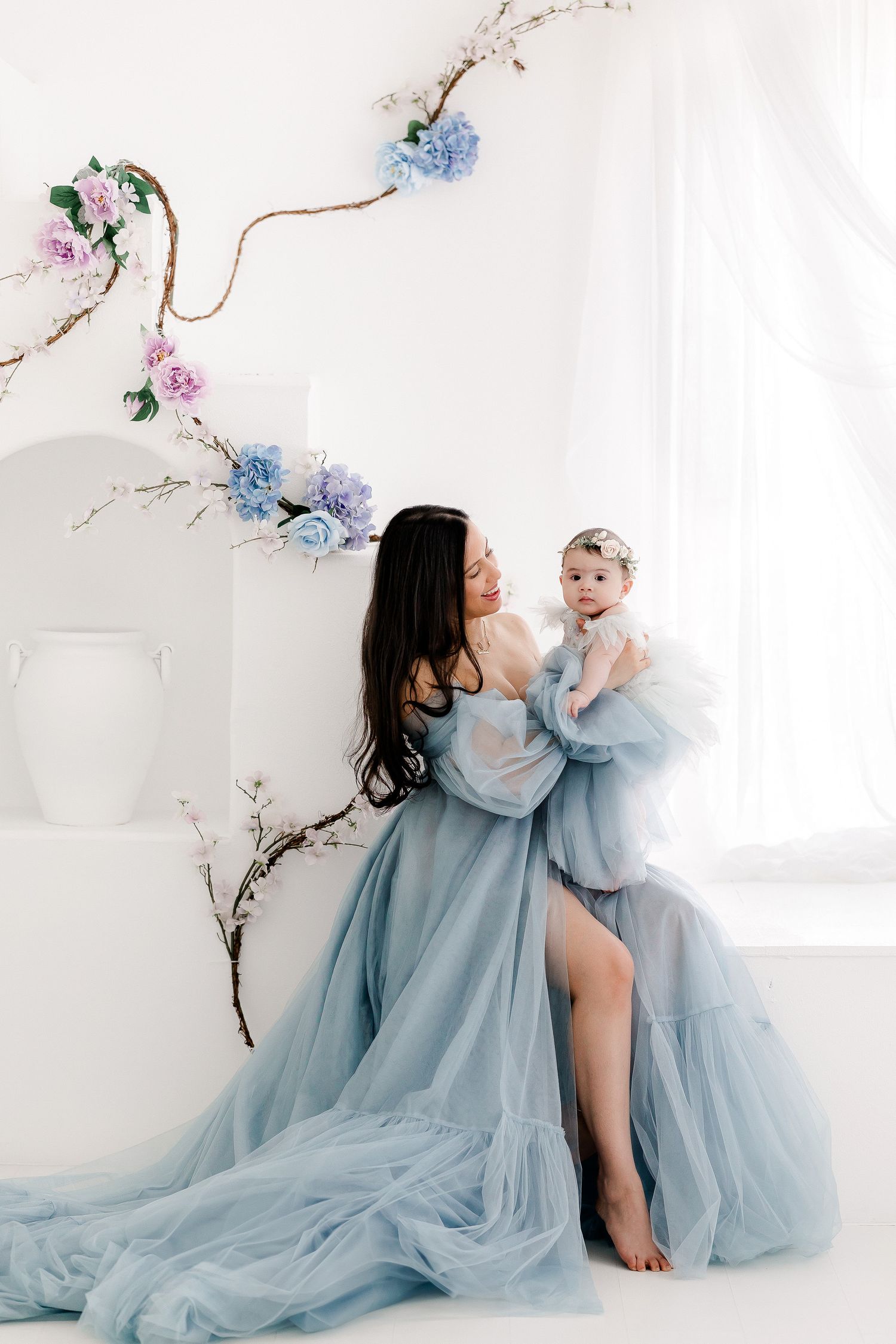 A tender moment captured in soft blue tulle dresses against a white backdrop with delicate floral branches.