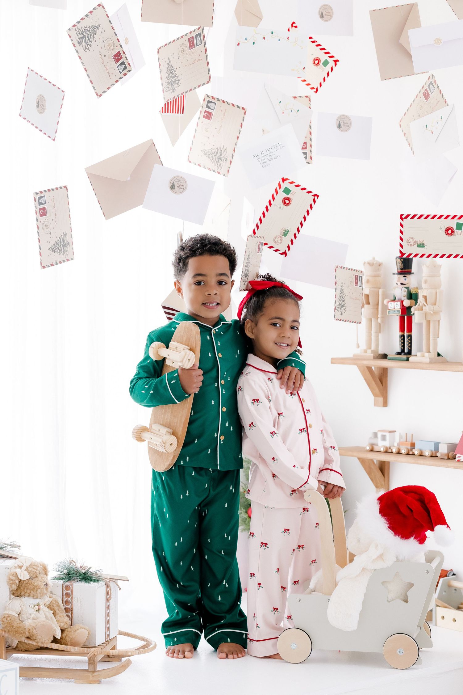 Two children in Christmas pajamas stand together surrounded by floating envelopes in a festive holiday decorated room.