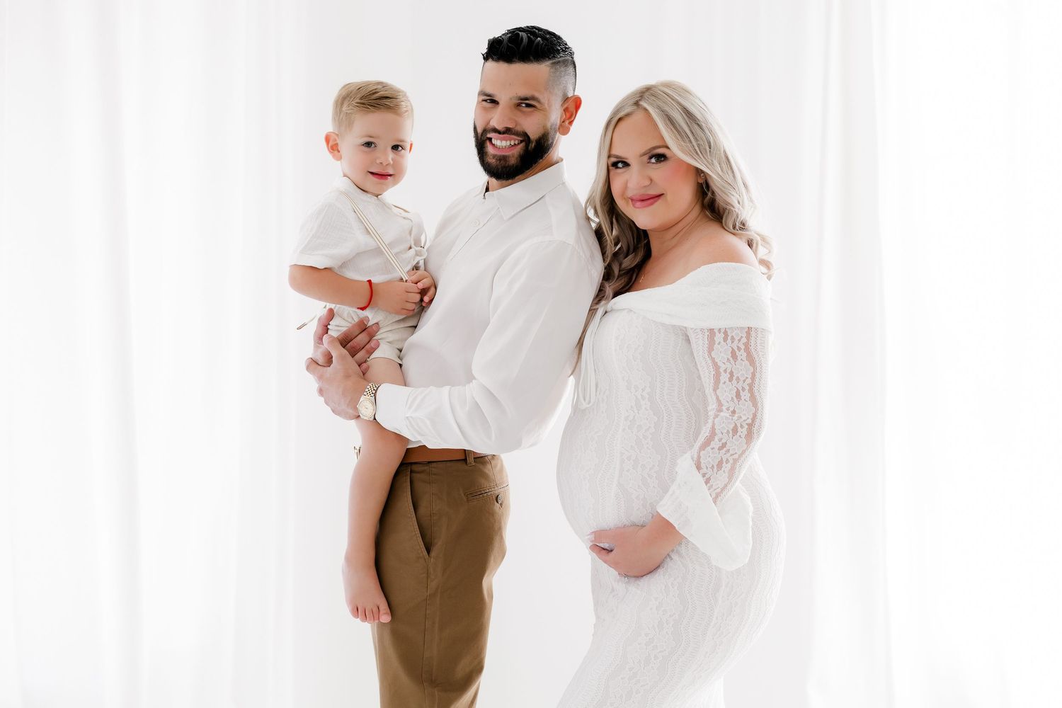 A family in white and brown outfits poses together against a white background for a studio portrait session.