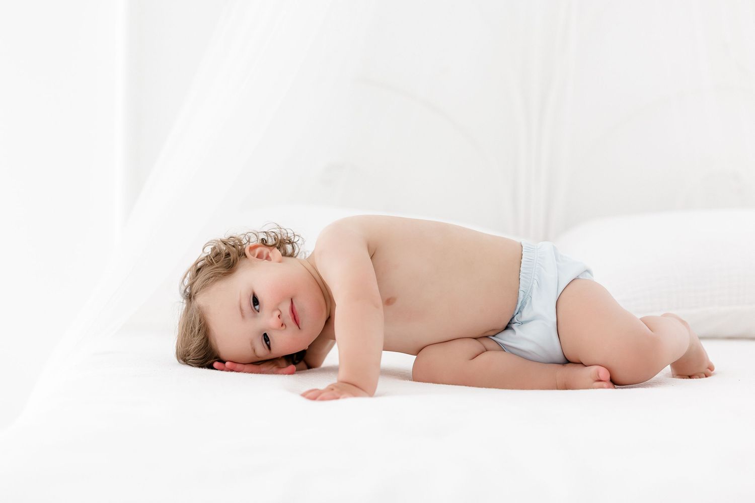 Baby in diaper lying on white blanket while playing and smiling with joy.