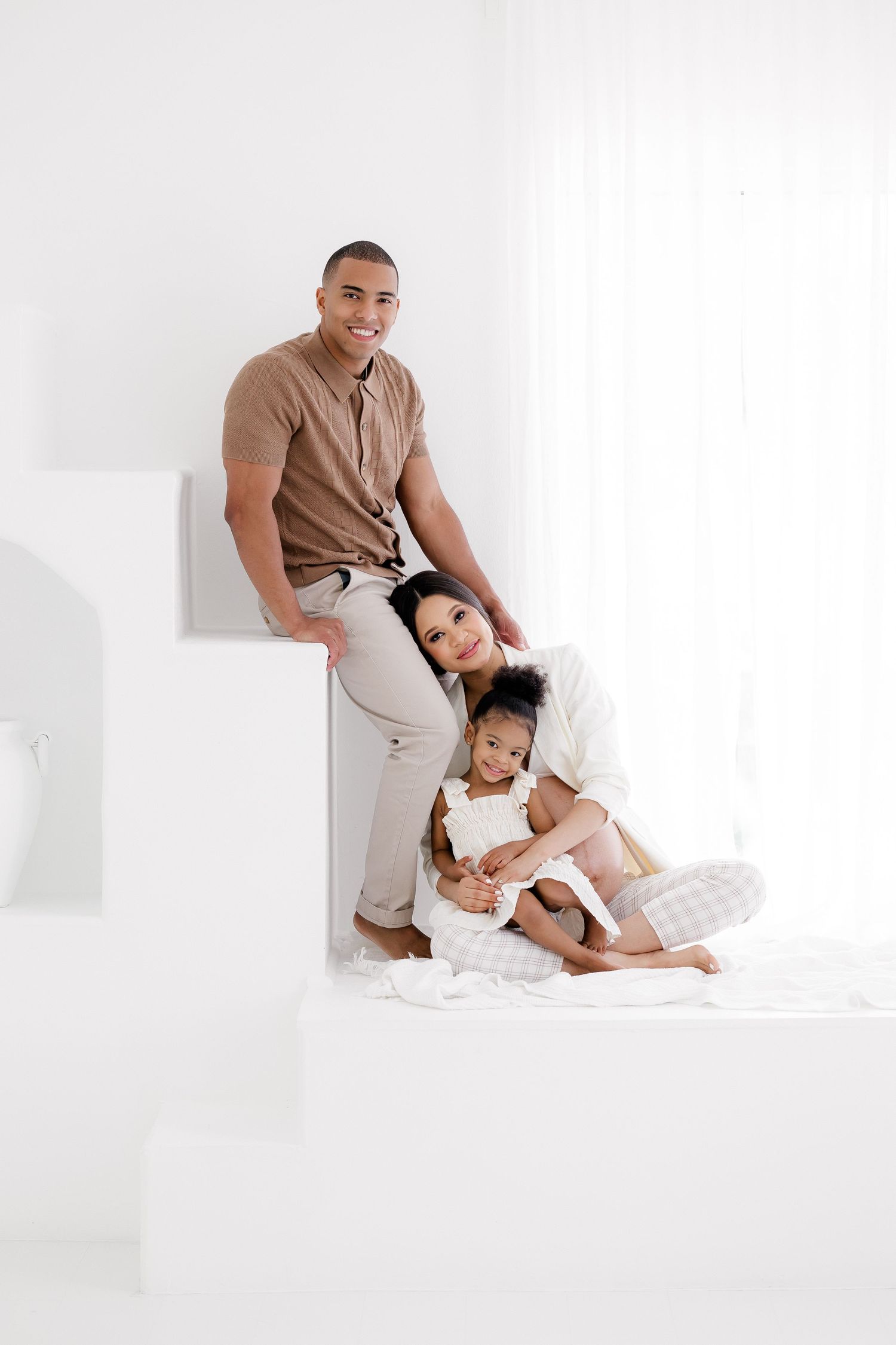 Intimate family maternity session with couple and child in neutral tones against white backdrop.