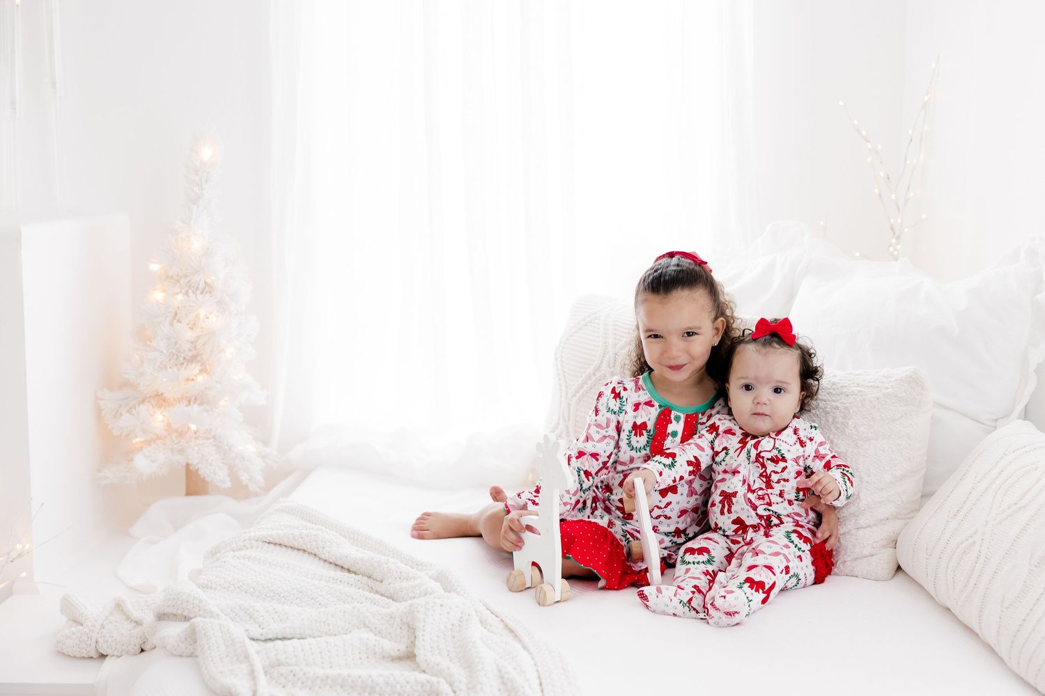 Festive Christmas morning scene with children in matching pajamas on white bedding.