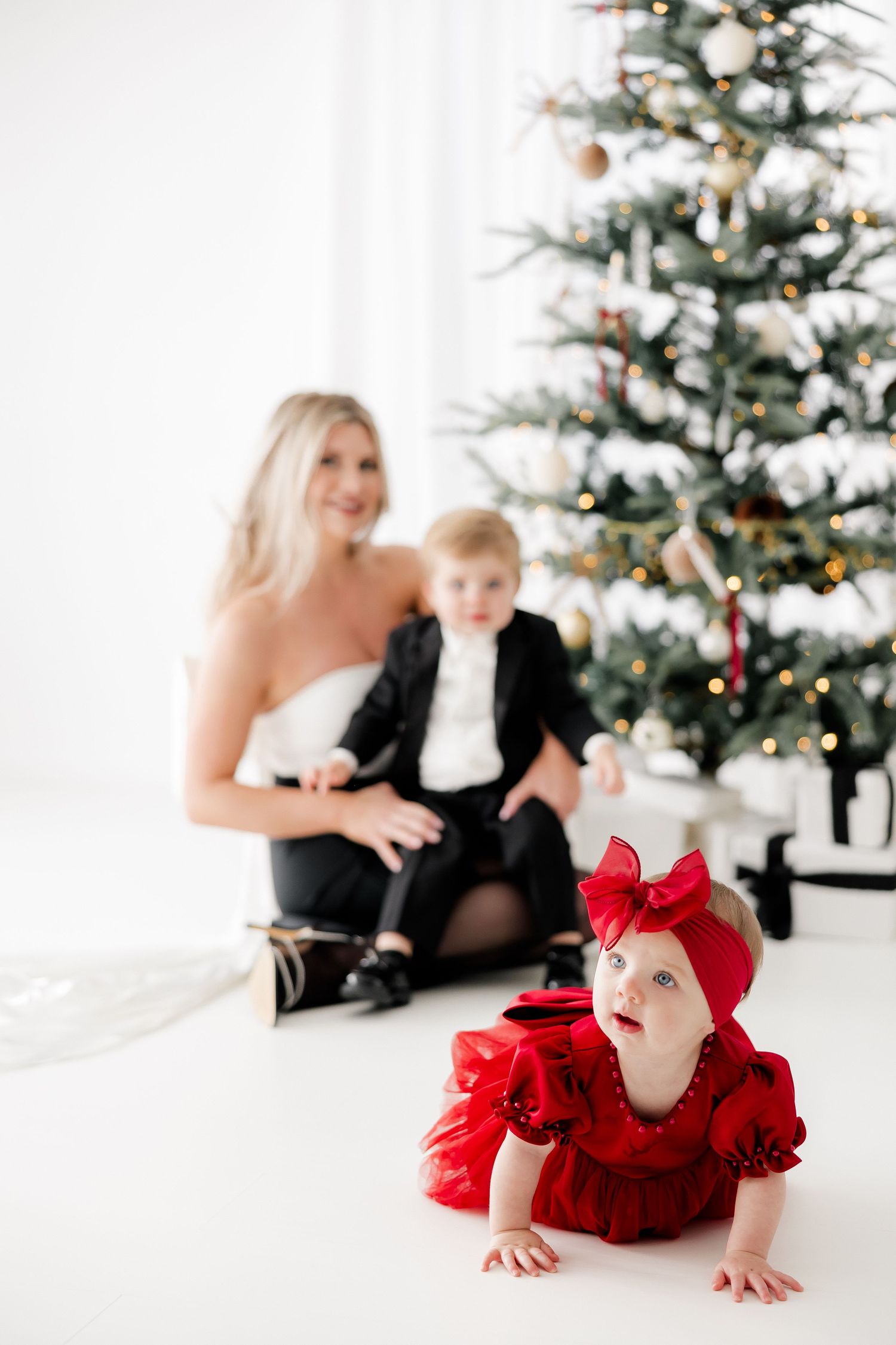 Christmas portrait setup with decorated tree and crawling baby in red dress.