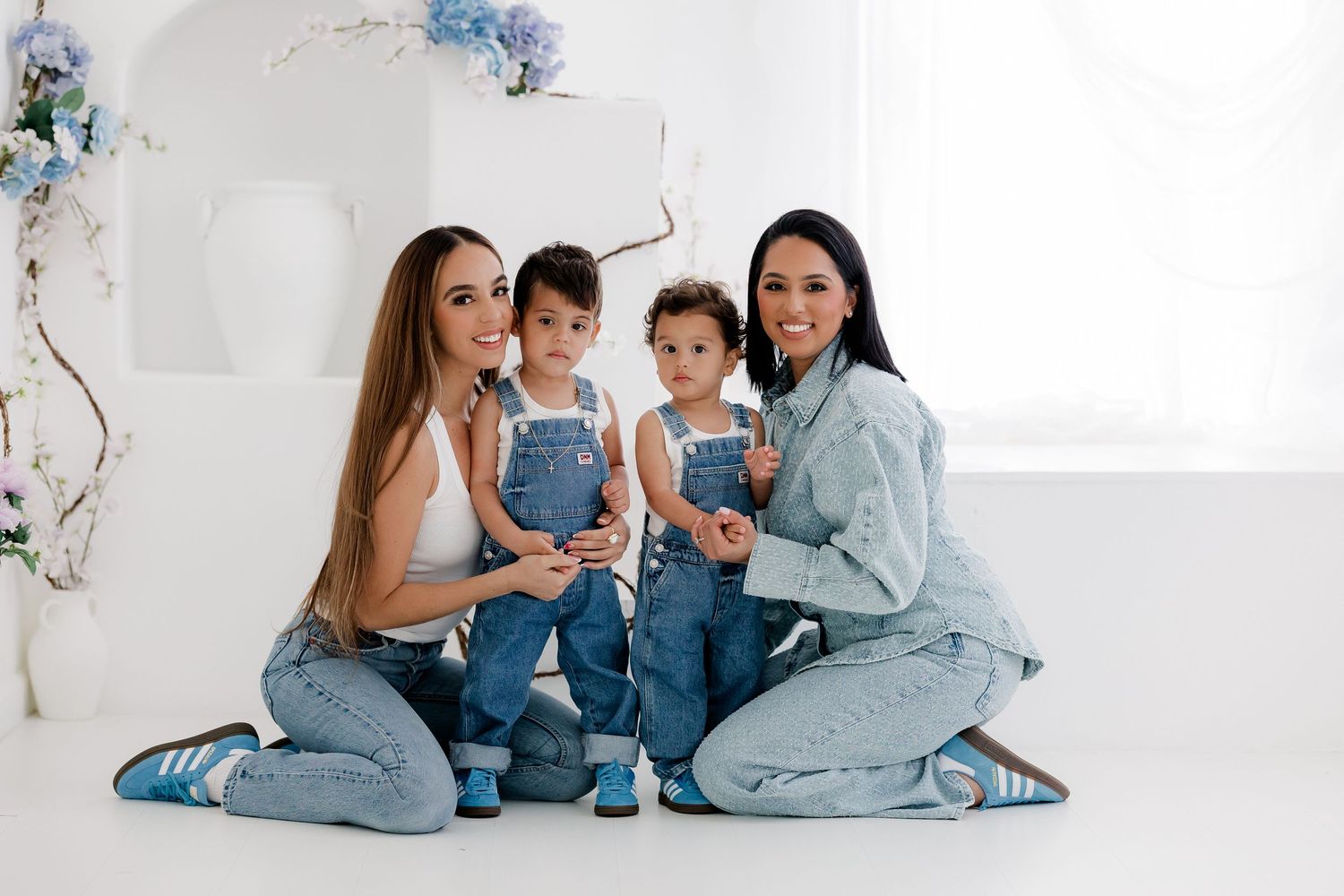 Family wearing matching denim outfits poses together in bright white studio setting for lifestyle photoshoot.