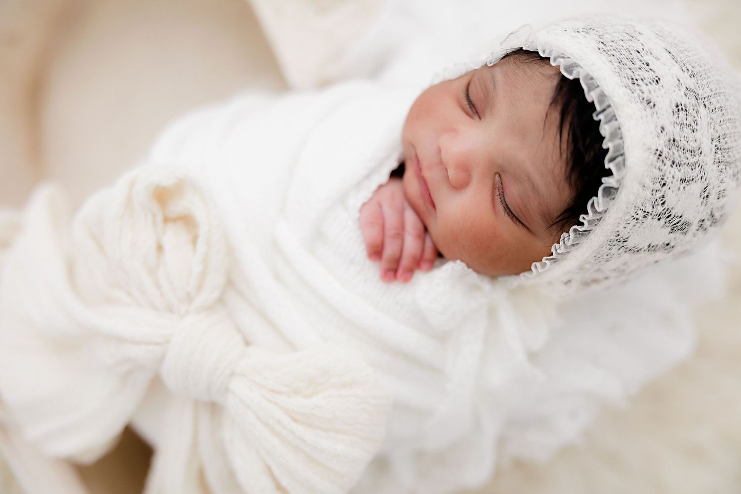 Classic newborn portrait in vintage-inspired lace bonnet on cream textured background.