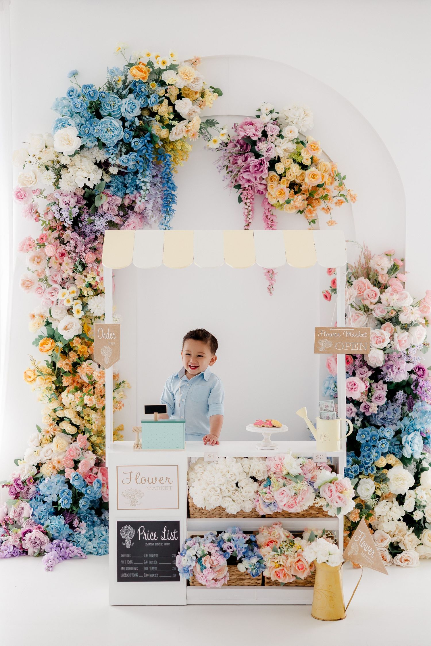 A floral photography studio setup with pastel blue and pink flower arches, chalkboard signs, and elegant white furniture.