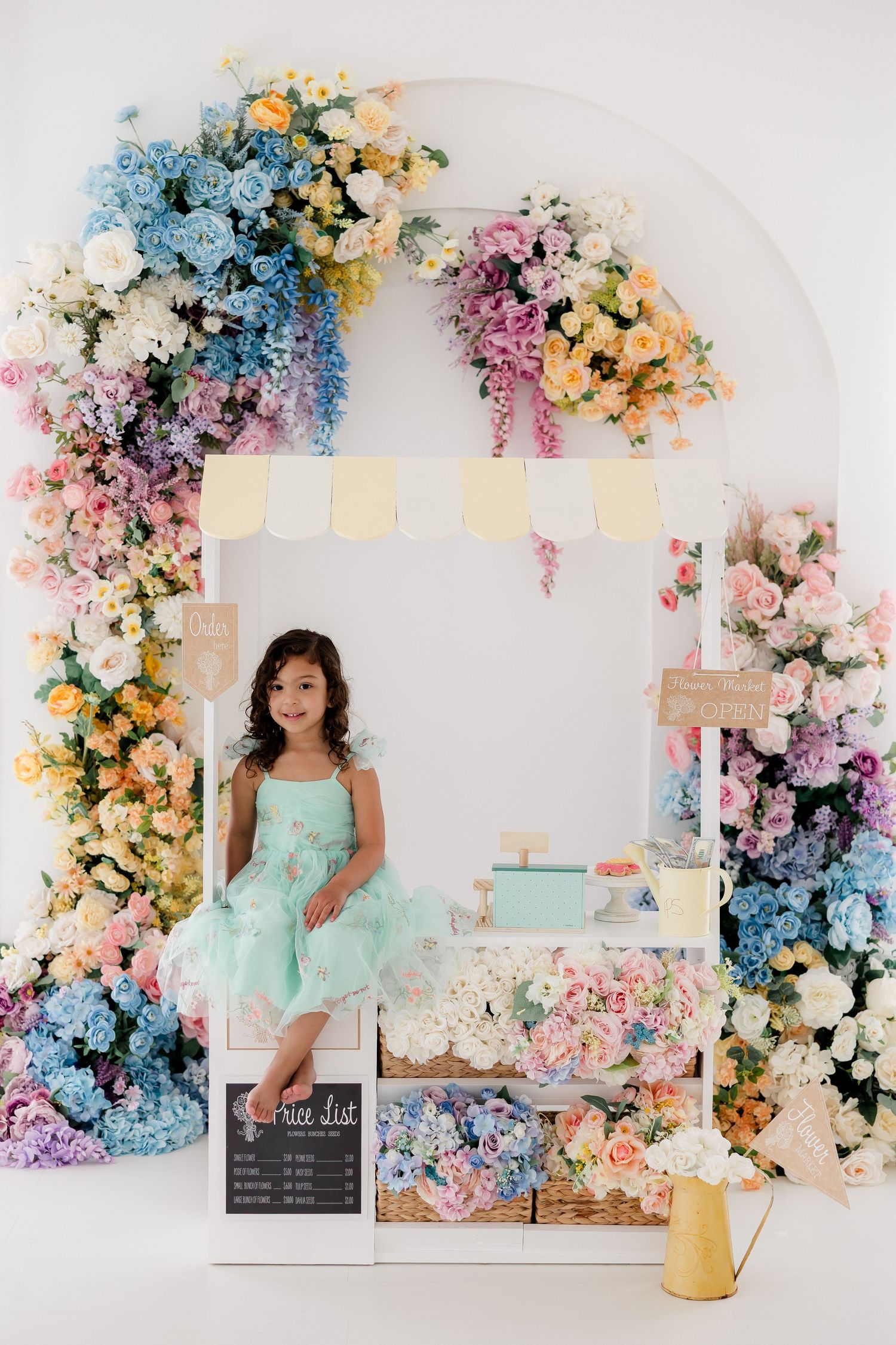Floral photography studio setup with pastel pink and blue flowers arranged in arches against white backdrop.
