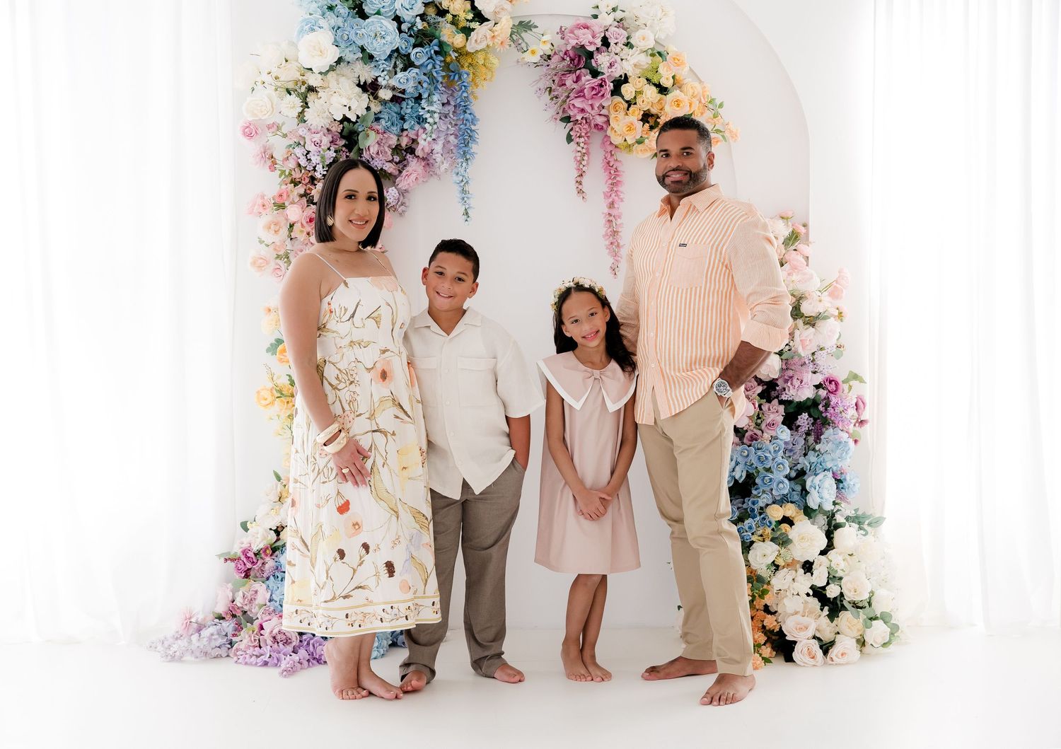 A family poses in front of a floral arch decorated with pink and blue flowers for a photo session.