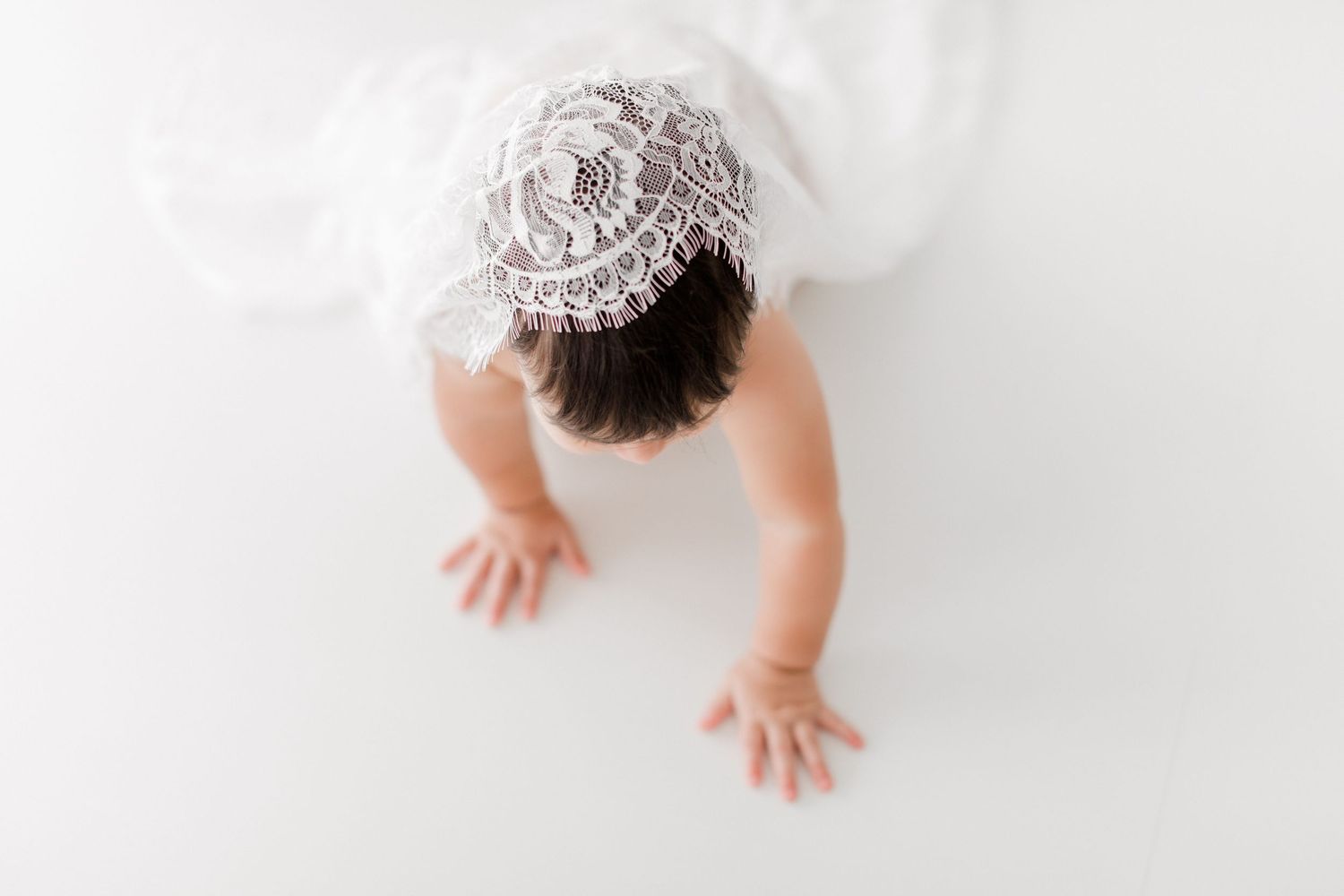 Baby crawling on white background wearing white onesie, showing progression of movement from left to right.