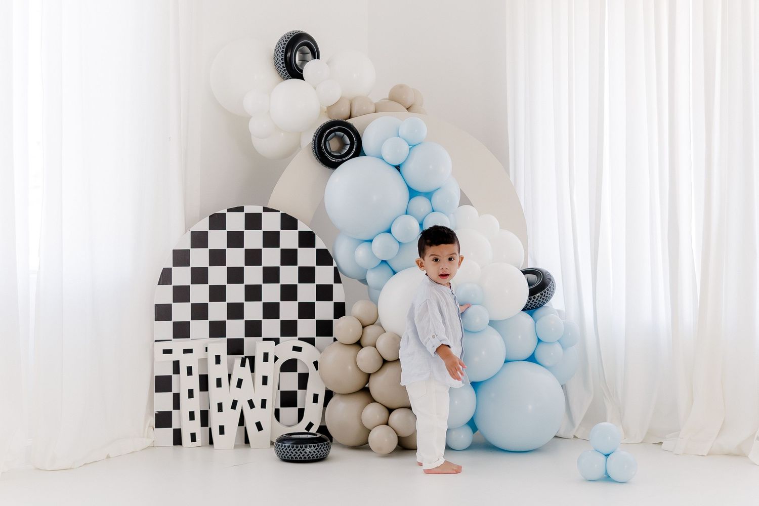 Baby birthday party setup with black and white checkerboard pattern, blue and beige balloon decorations in a white room.