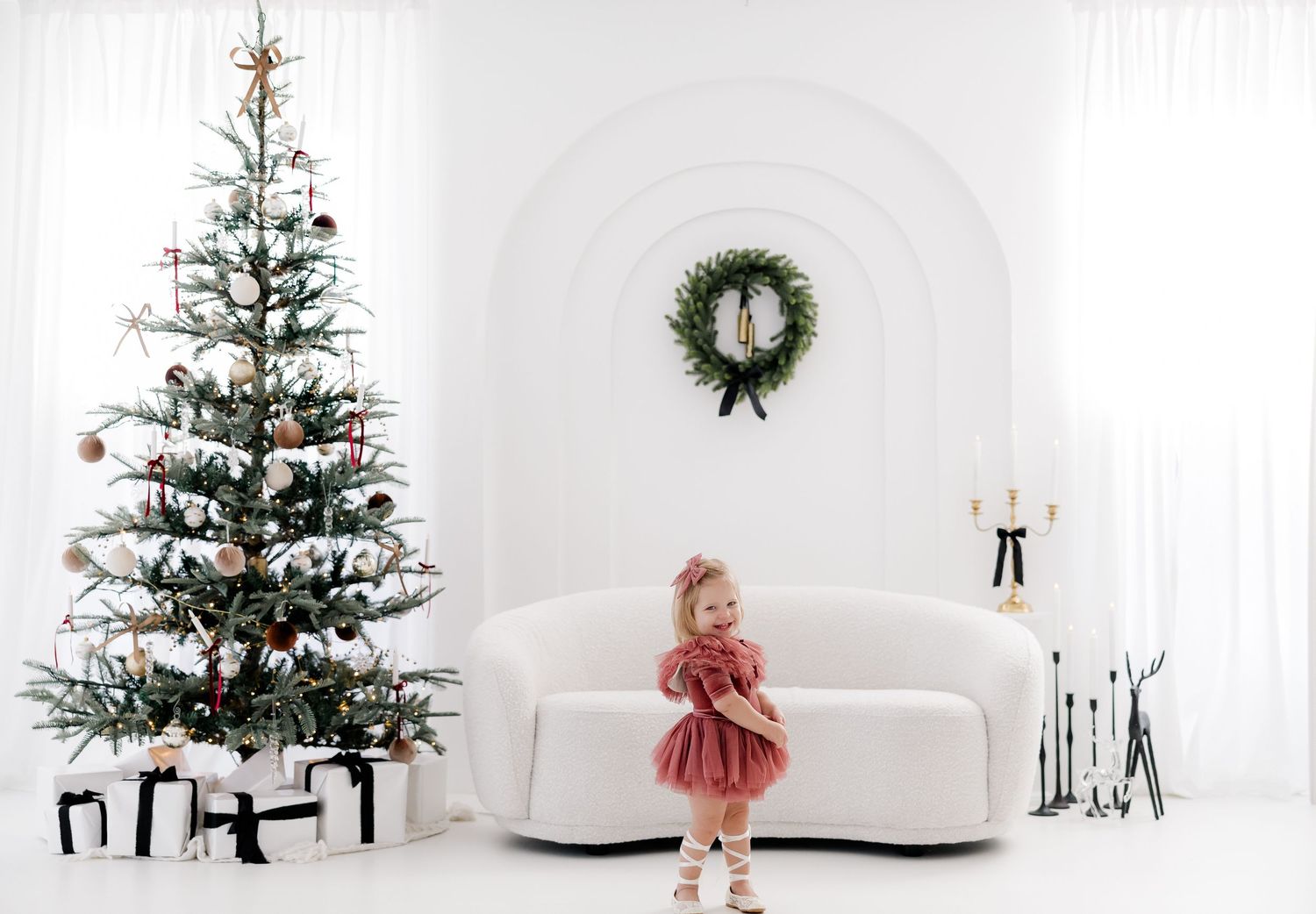 A decorated Christmas tree stands in an elegant white room with a matching wreath and holiday decor.