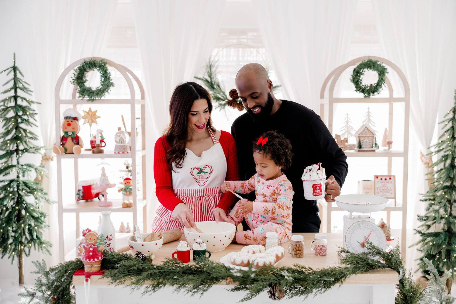 Family gathered around a white table decorated with Christmas greenery and holiday treats.