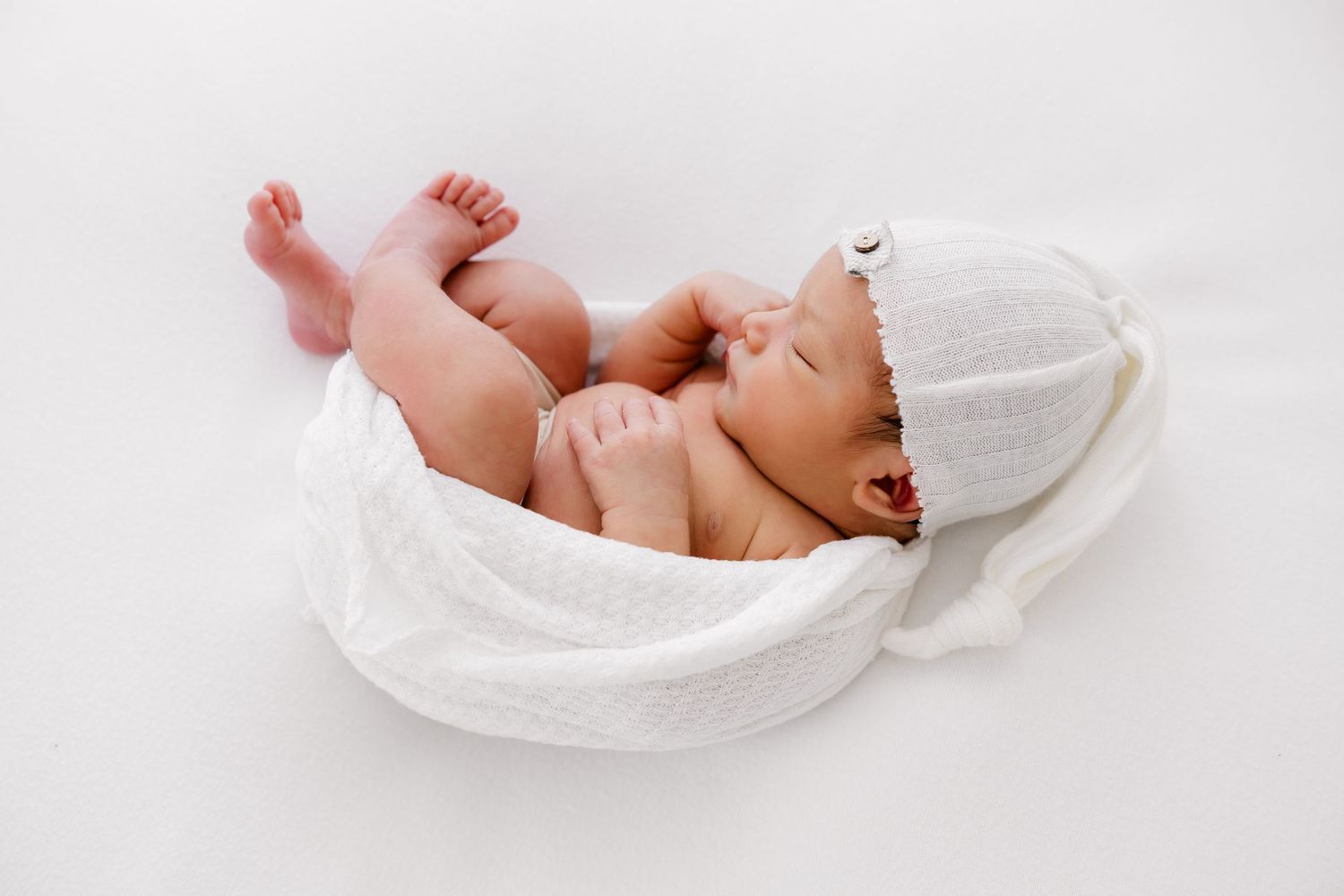 A series of four images showing a newborn baby wrapped in white fabric against a light background.