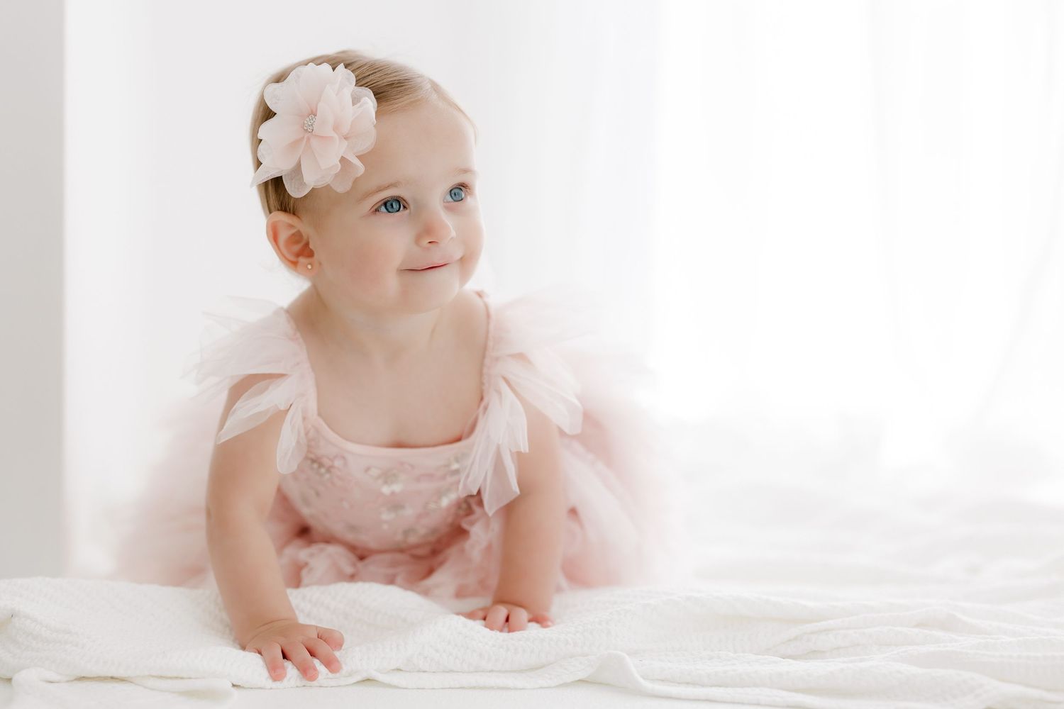 Baby in pink tulle dress crawling on white floor during photo session.