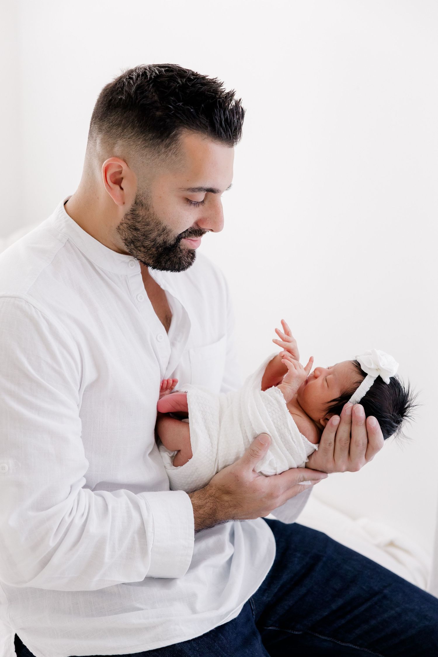 Parent in white shirt cradles newborn baby against white background.