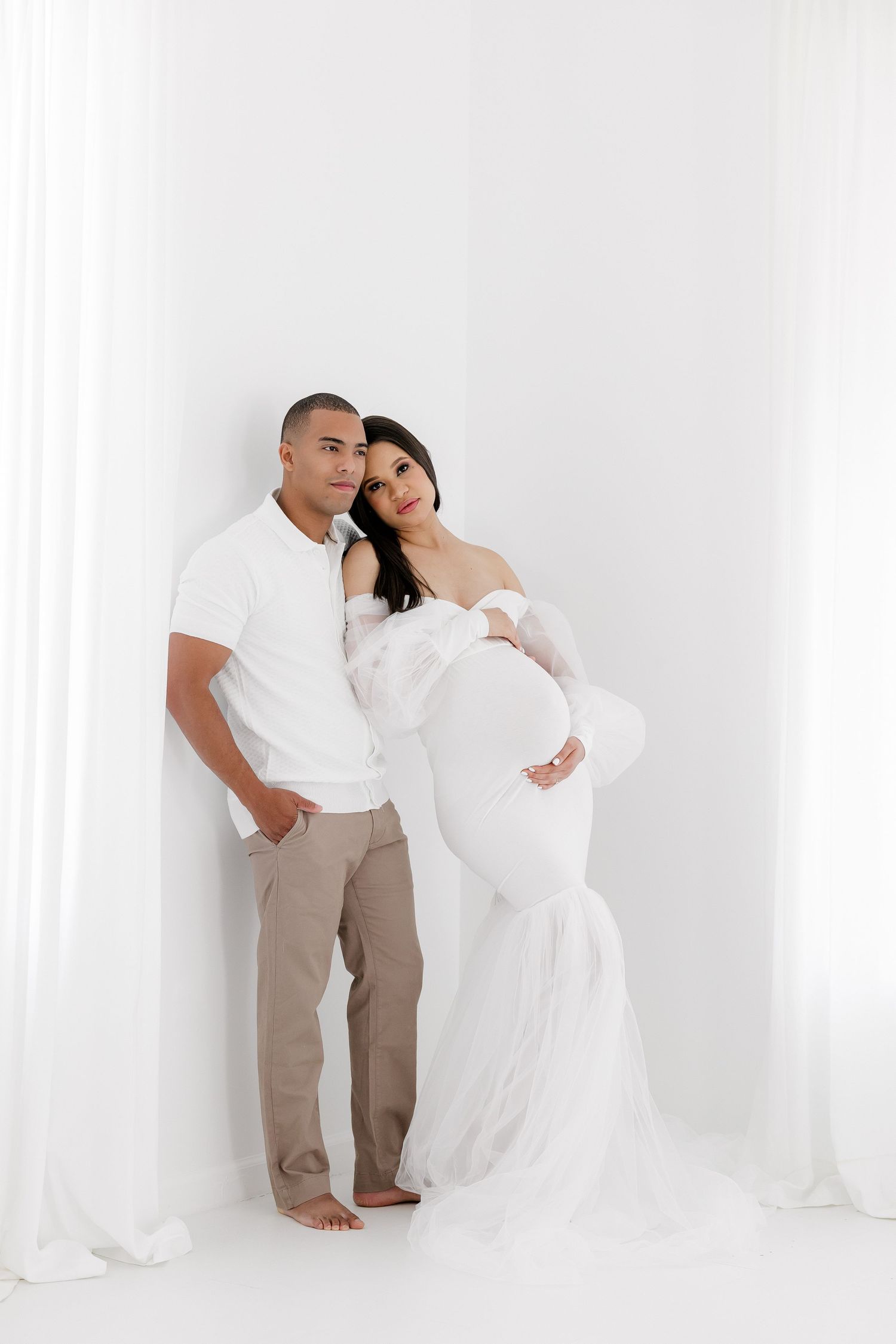 Intimate couple's maternity photoshoot against white backdrop.