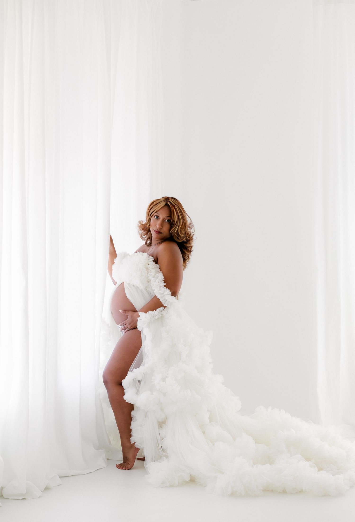 Artistic maternity portraits with billowing white fabric in minimalist studio setting.