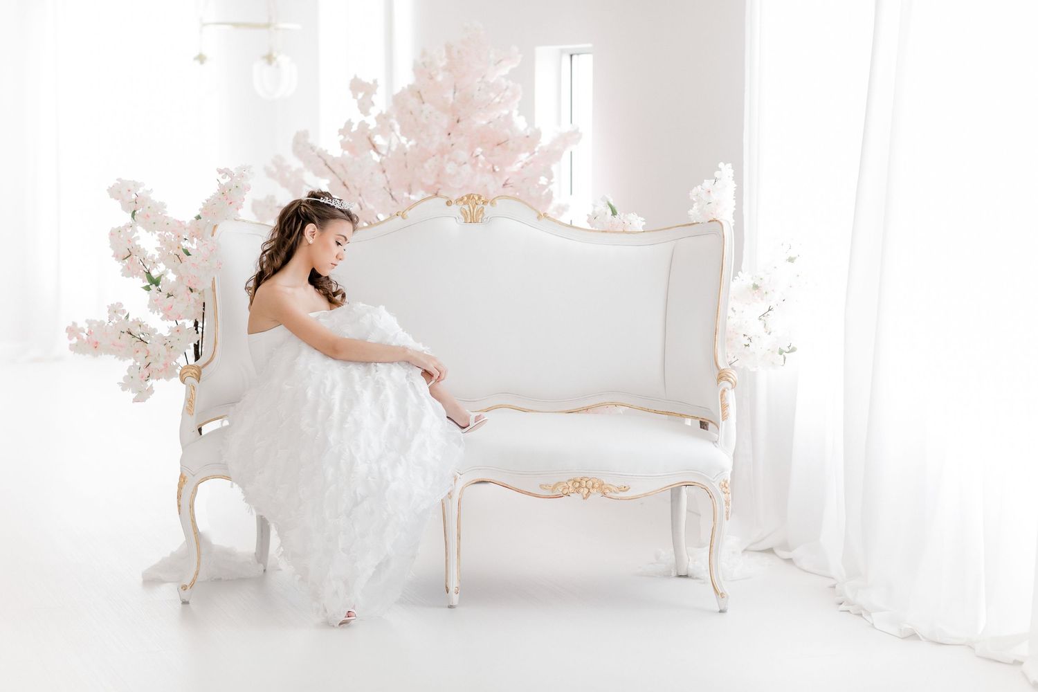 Elegant white bridal scene with vintage French settee and soft pink floral decorations in bright ethereal setting.