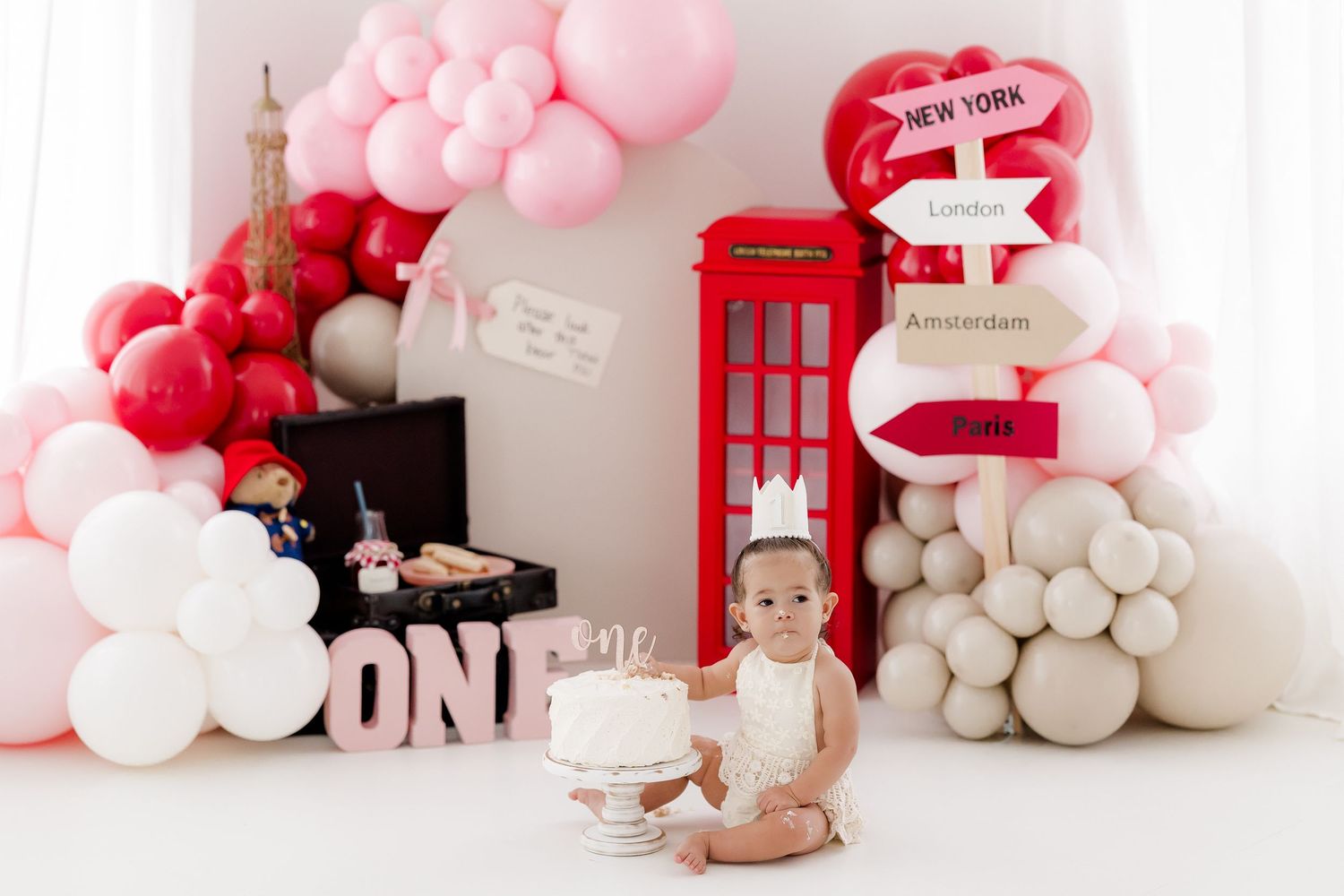 Pink and red balloon arch decorates a party space with London-themed elements including a red telephone booth.