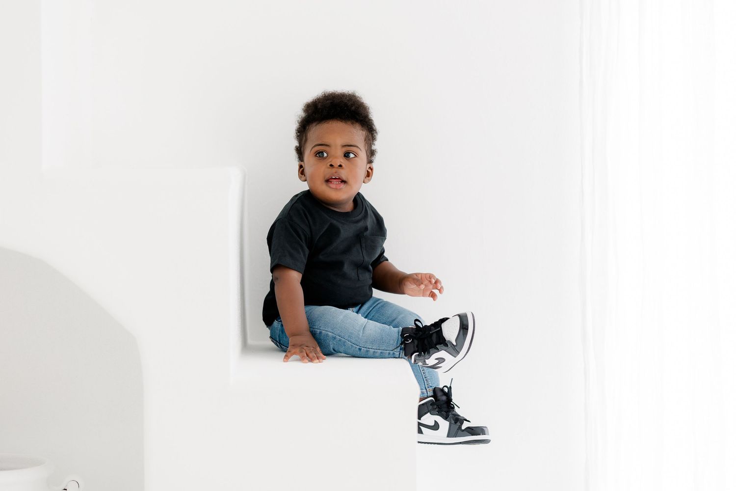 Baby in denim and sneakers poses on a white backdrop in multiple adorable candid shots.