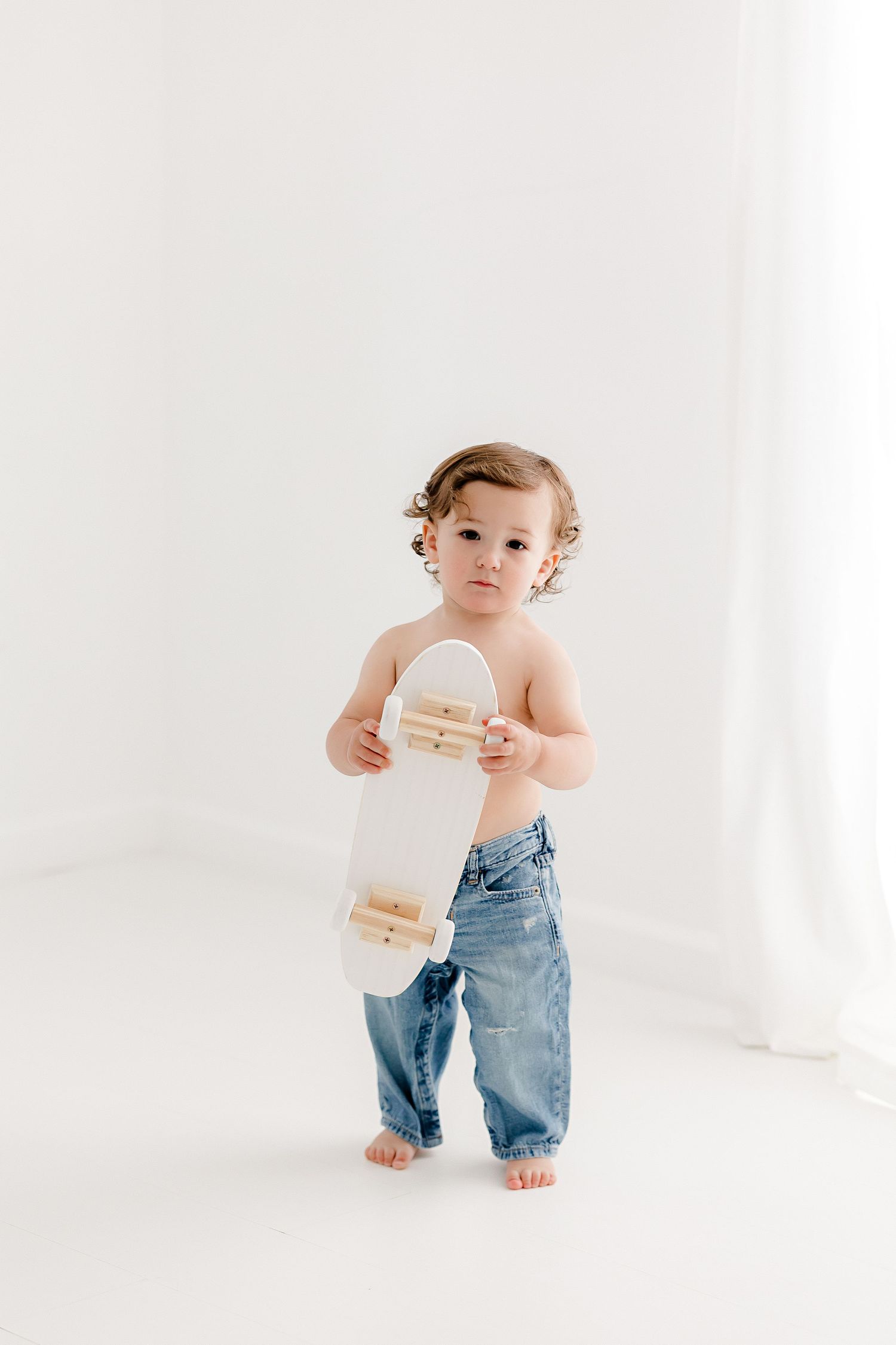 Adorable baby wearing denim overalls crawls and plays in minimalist white studio setting.