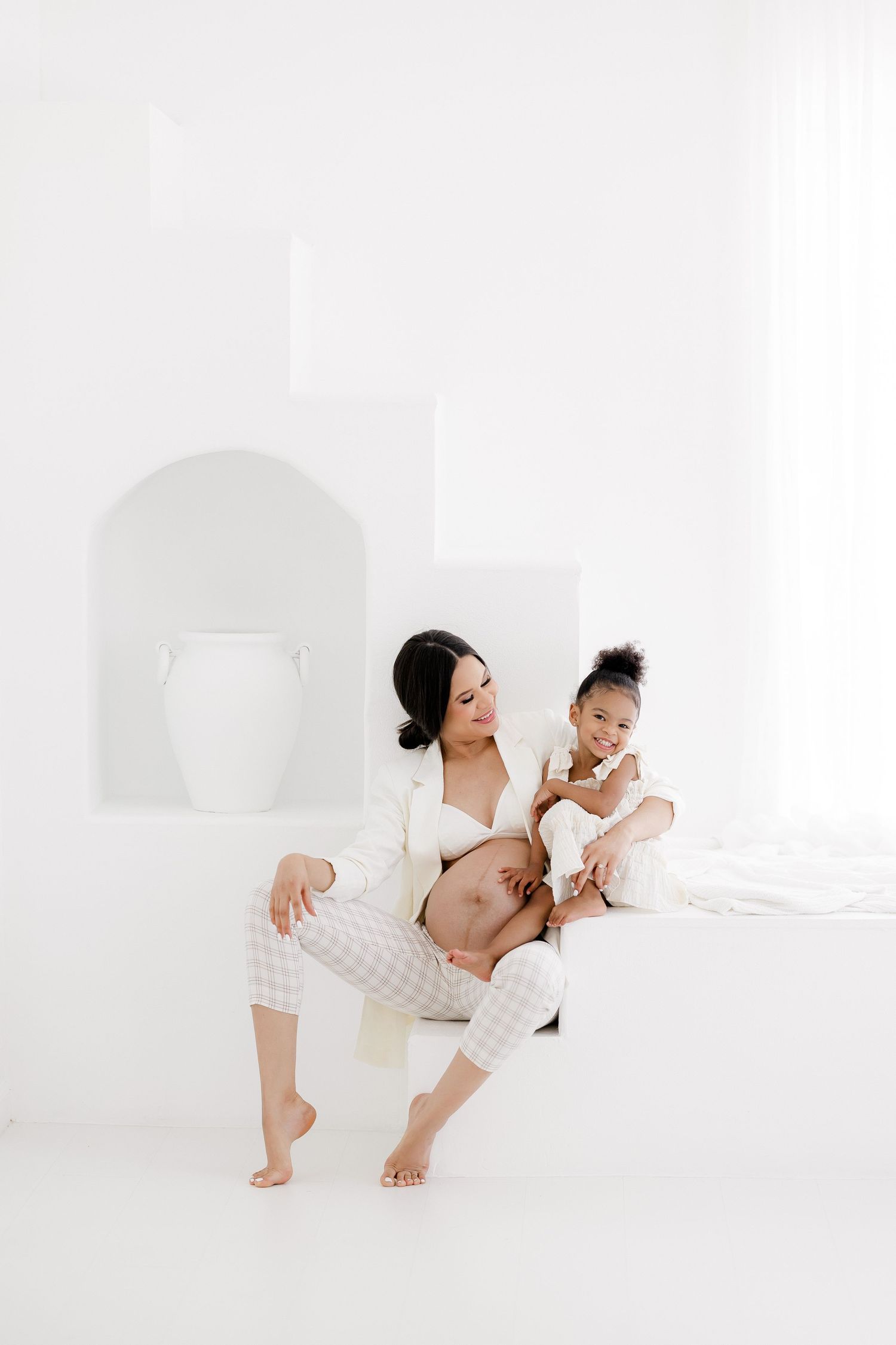 Playful family maternity photos with parents and child in white studio setting.