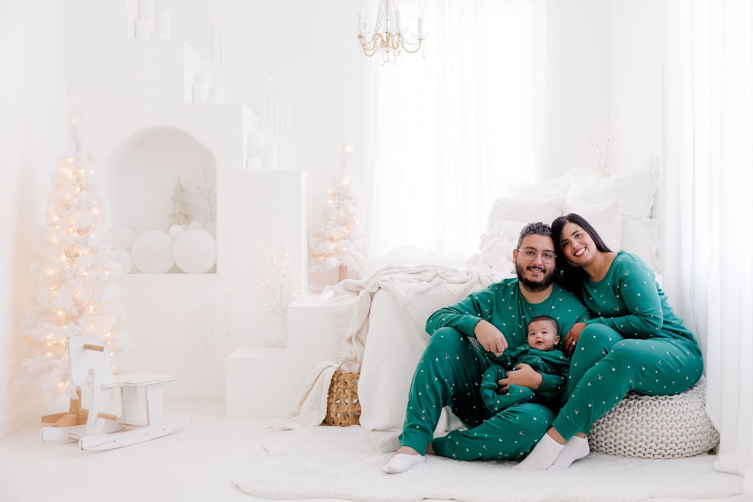 Family wearing matching green pajamas sitting together in white holiday themed room.