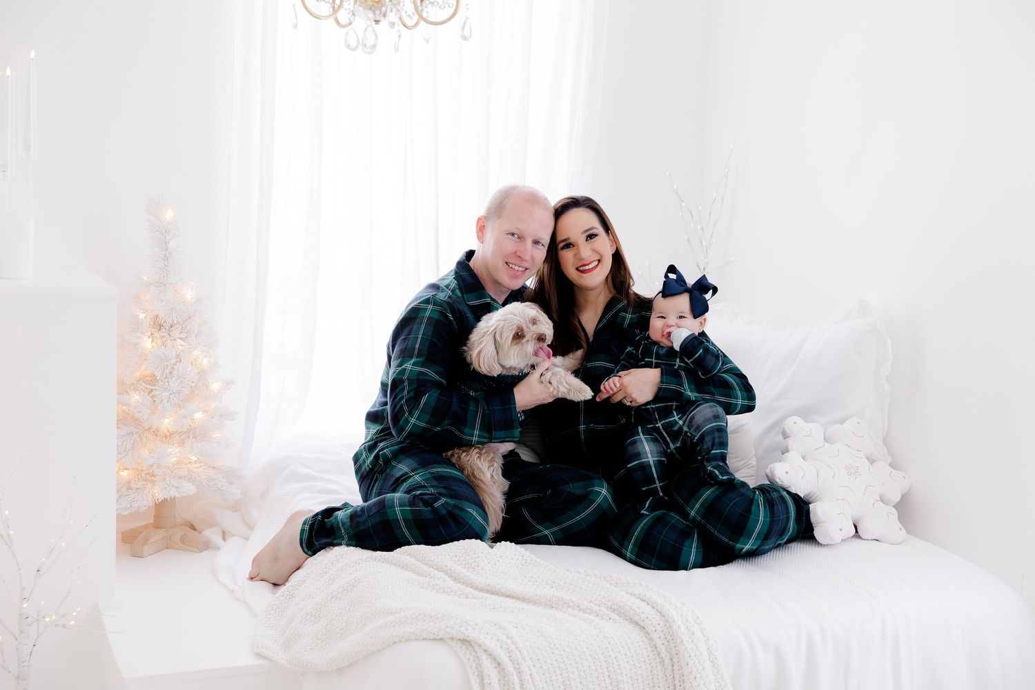 Family lounging together on white bedding during holiday photo session.