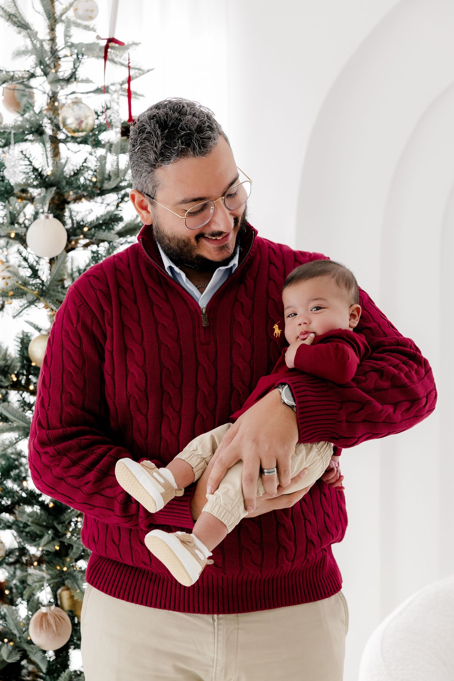 Father and baby wearing matching burgundy sweaters embrace during holiday photoshoot.