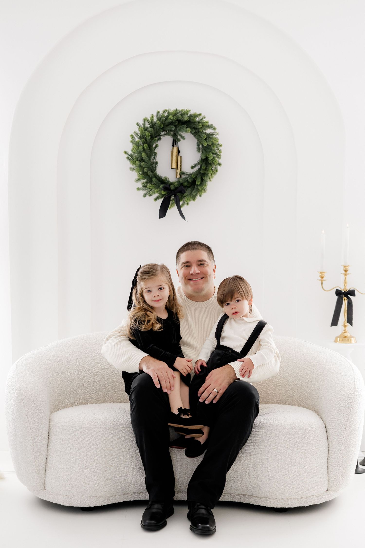 Family portrait on white couch with holiday wreath and white Christmas decor.