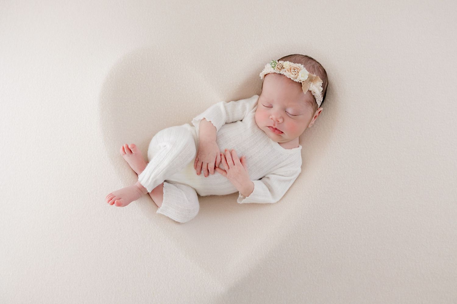 Sweet newborn photography session featuring tiny baby in white outfit on light backdrop.