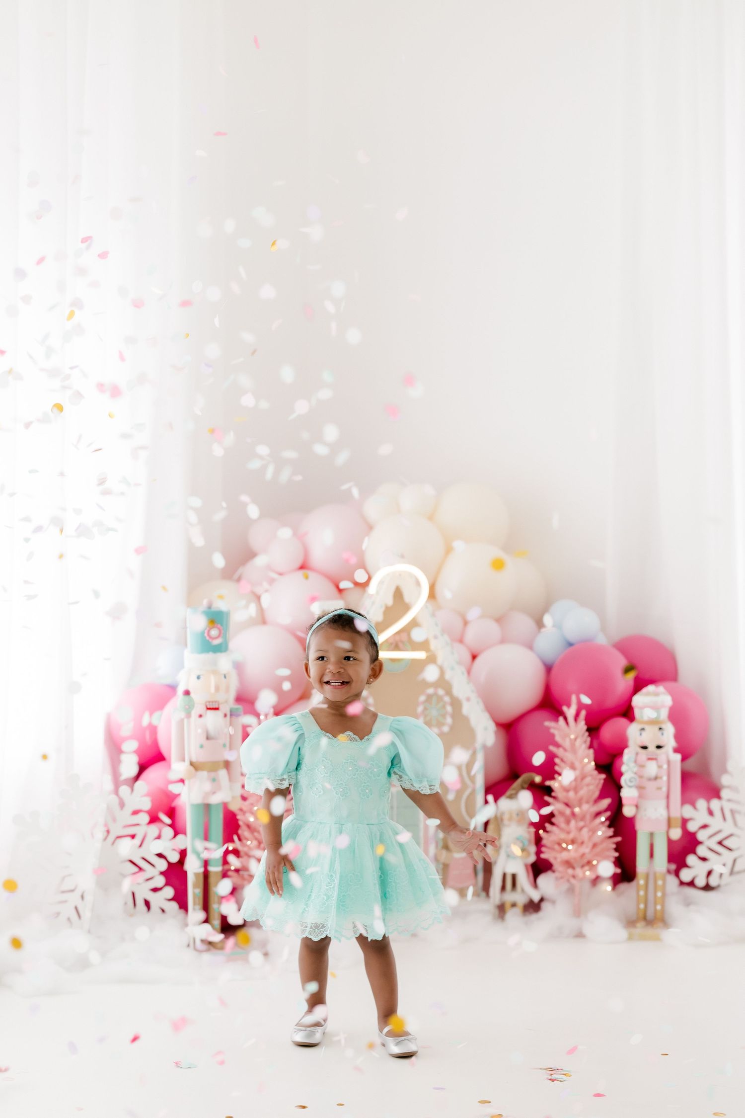 Sweet celebration photoshoot with mint green dress against pink and white balloon backdrop with confetti.