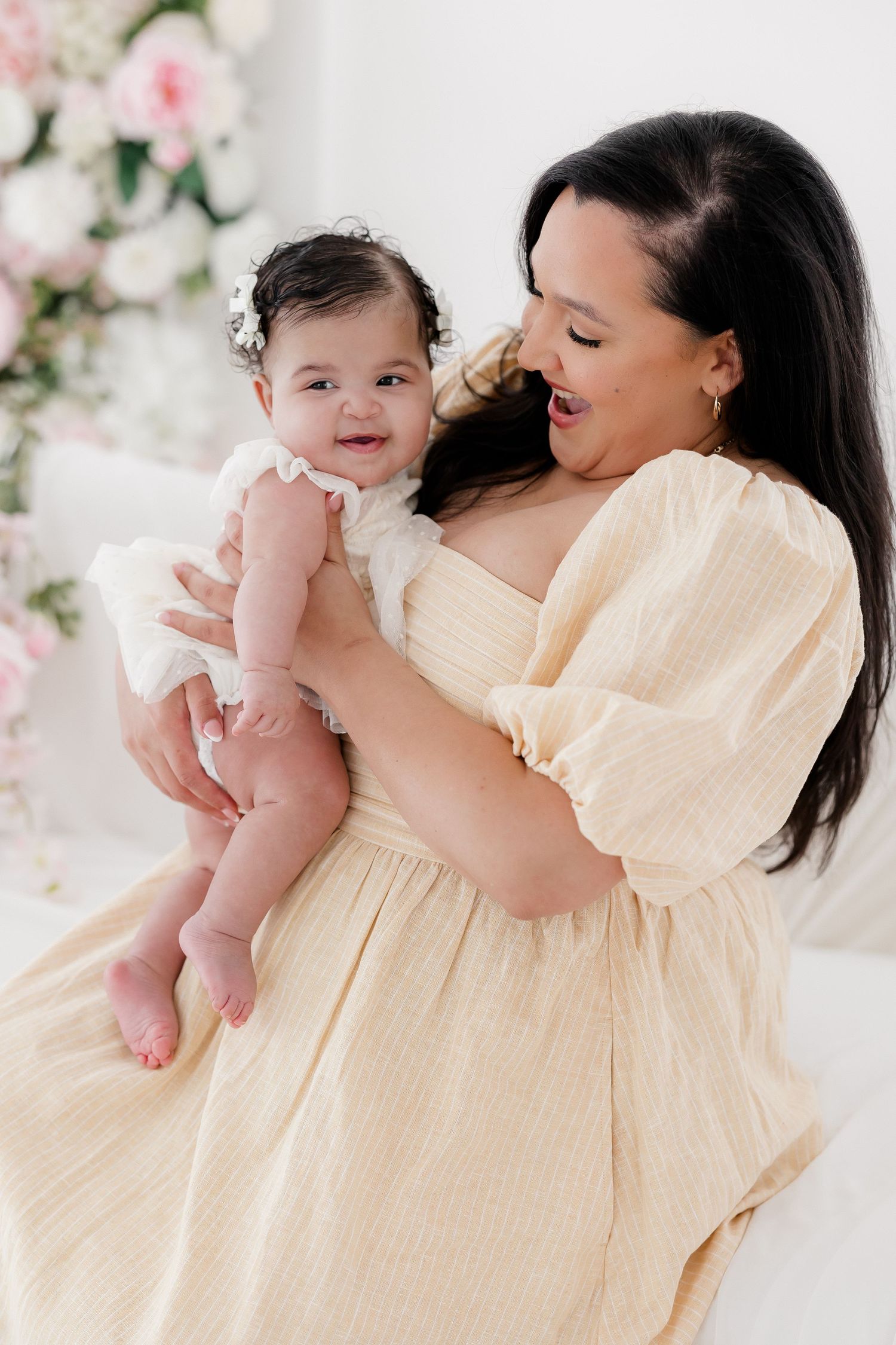 A tender moment captured in cream-colored dresses against a floral backdrop with soft pink and white blooms.