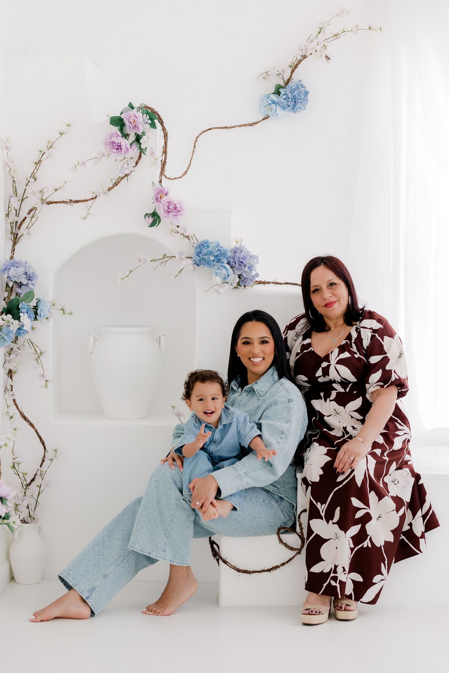 Family wearing matching light blue and brown floral outfits poses together against white backdrop with delicate floral decor.