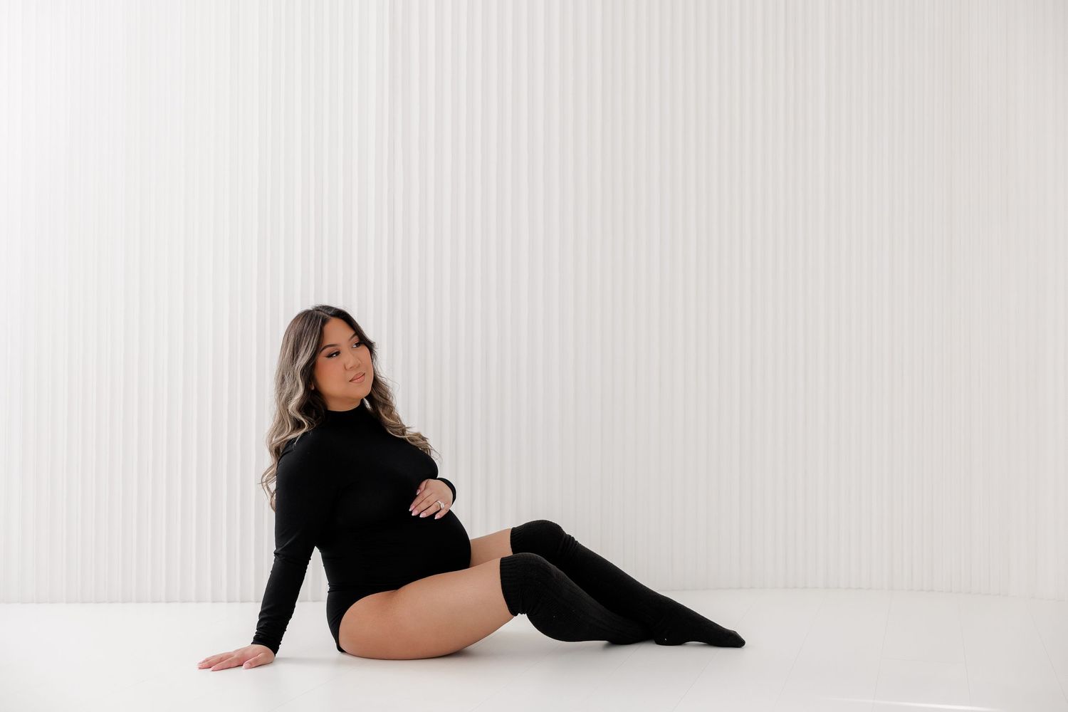 Minimalist maternity photos in black bodysuit against white studio backdrop.