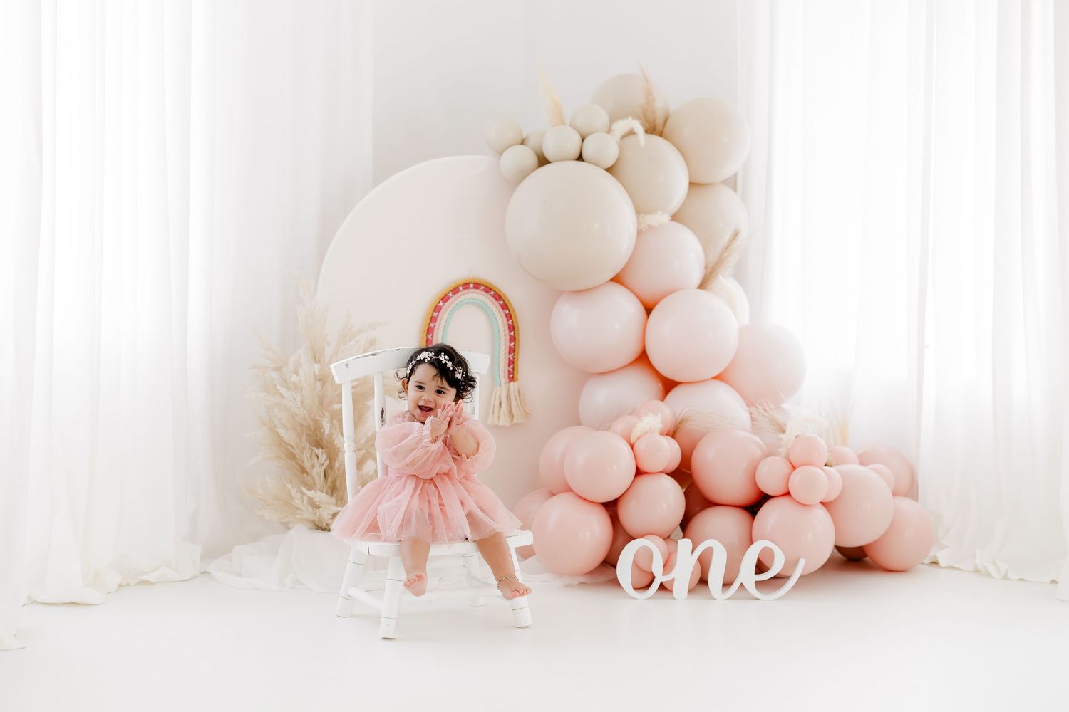 Elegant pink and white balloon arch with floral decorations against a light backdrop.