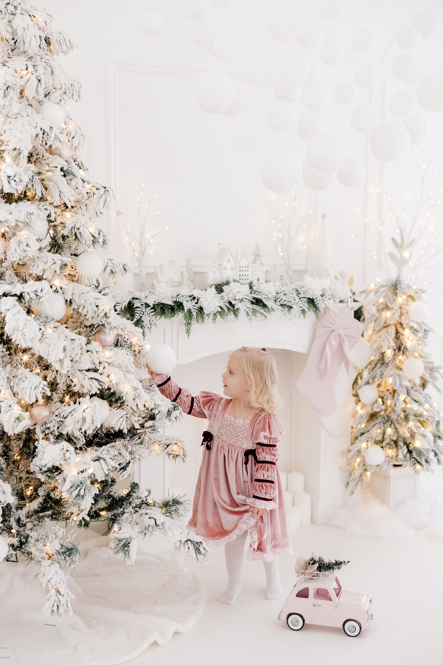 Winter wonderland studio setup with flocked trees, pink scooter, and holiday decorations.
