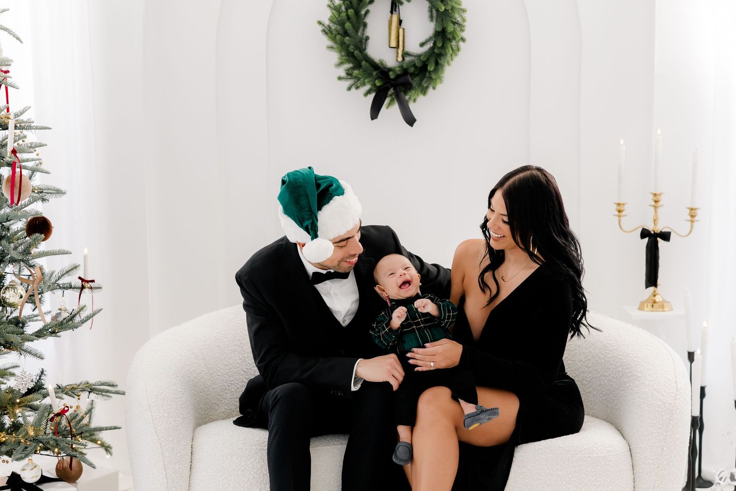 Holiday family portrait session in modern white studio with Christmas wreath and decorative elements.
