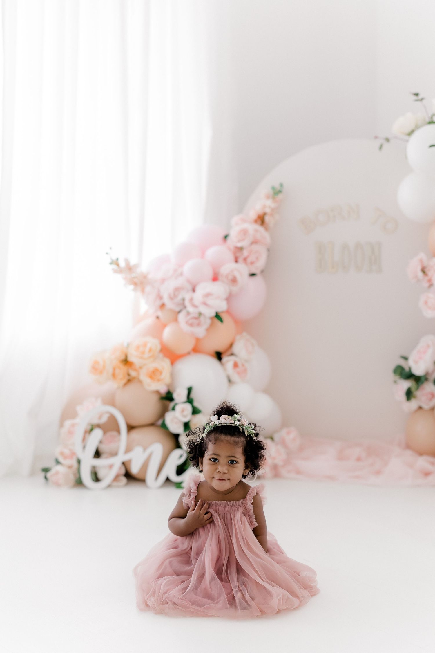Studio photography setup with pink balloon arch and floral decorations.