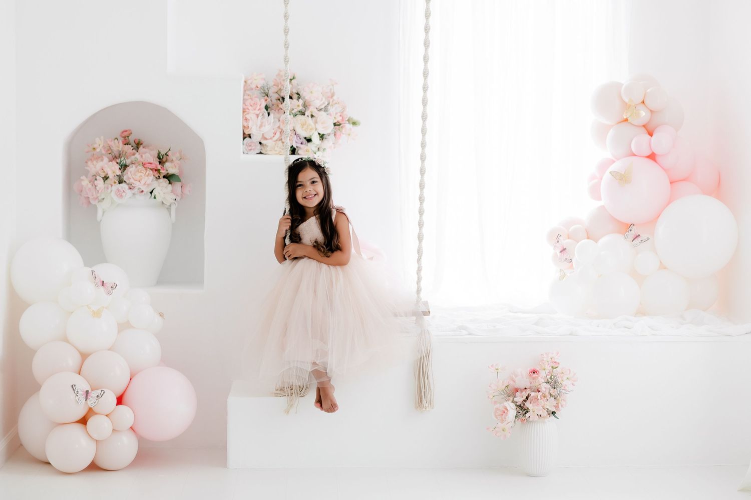 Pink and white balloon decorations create a dreamy backdrop for a romantic photo session in a bright studio space.