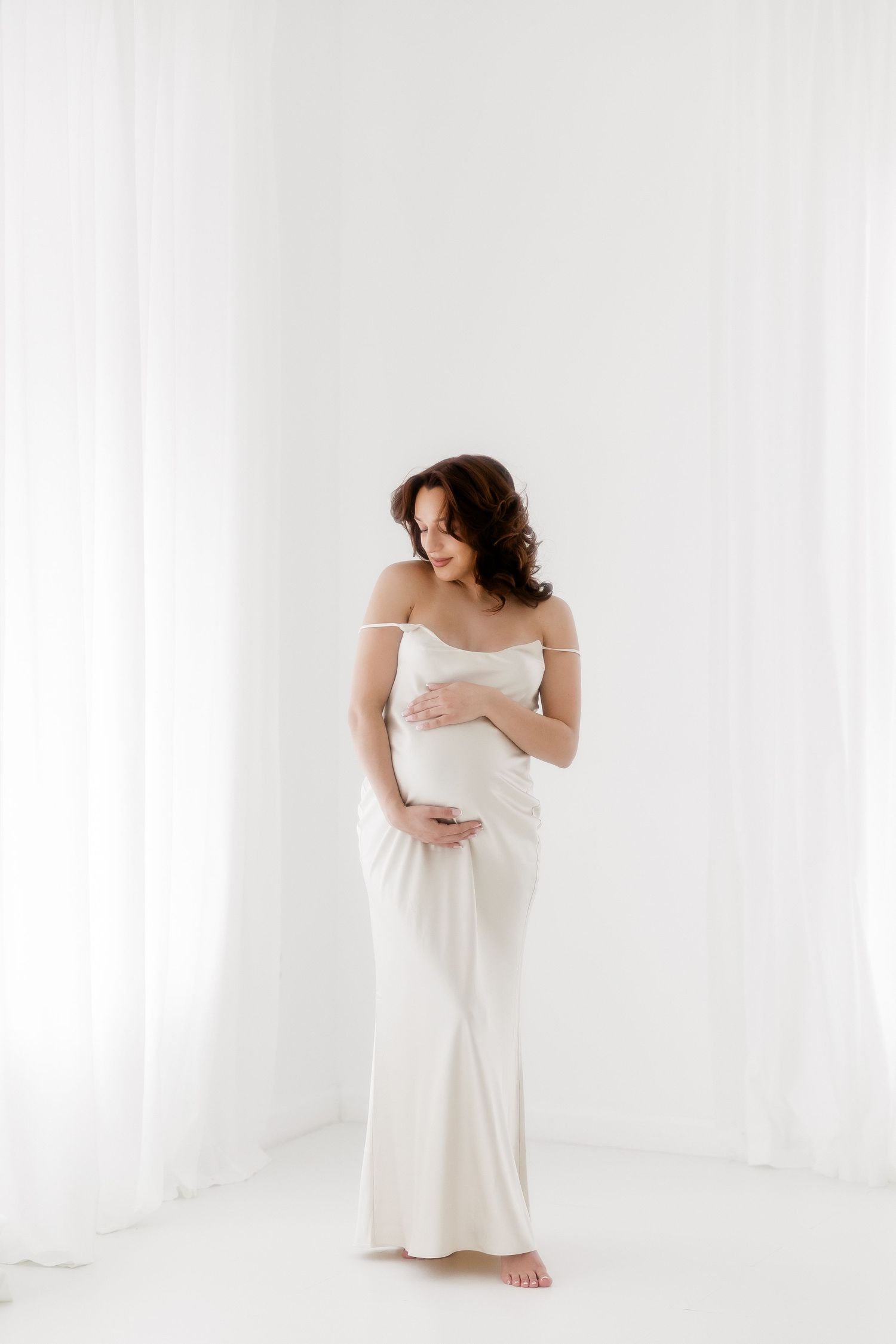 Ethereal artistic portrait of figure wrapped in white fabric against bright minimalist background in studio setting.