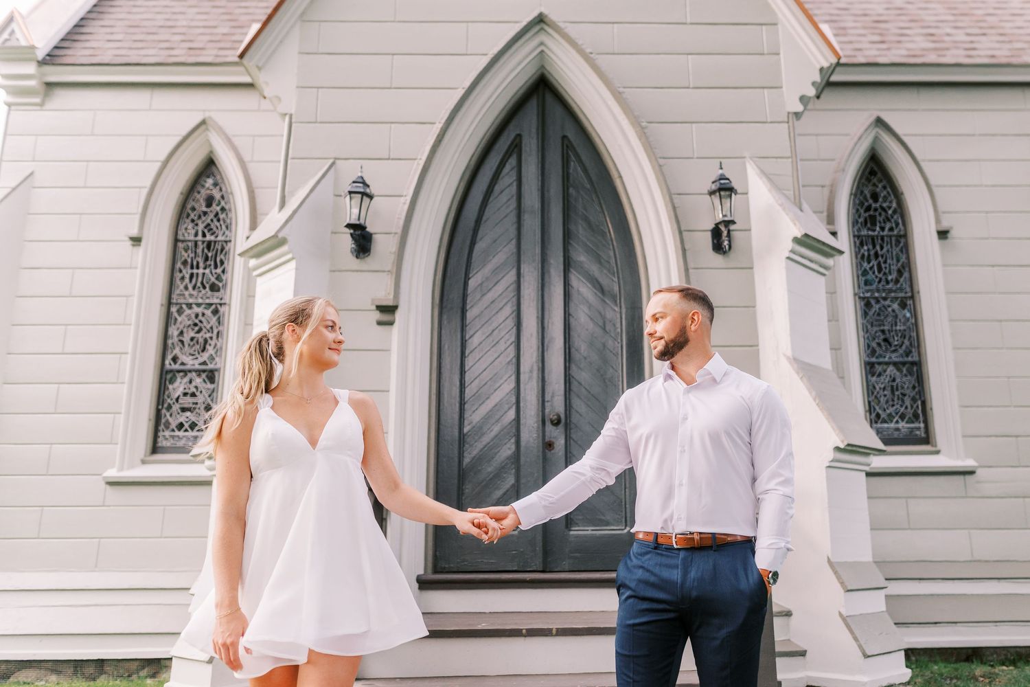A couple shares romantic moments and poses outside a beautiful stone church with arched Gothic windows and doorways.