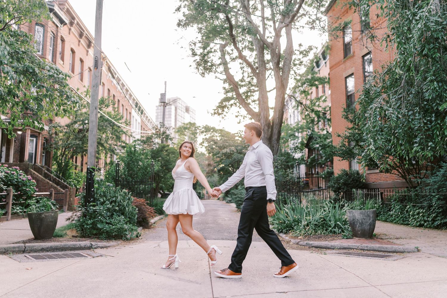 A couple dances playfully together on a tree-lined cobblestone city street.
