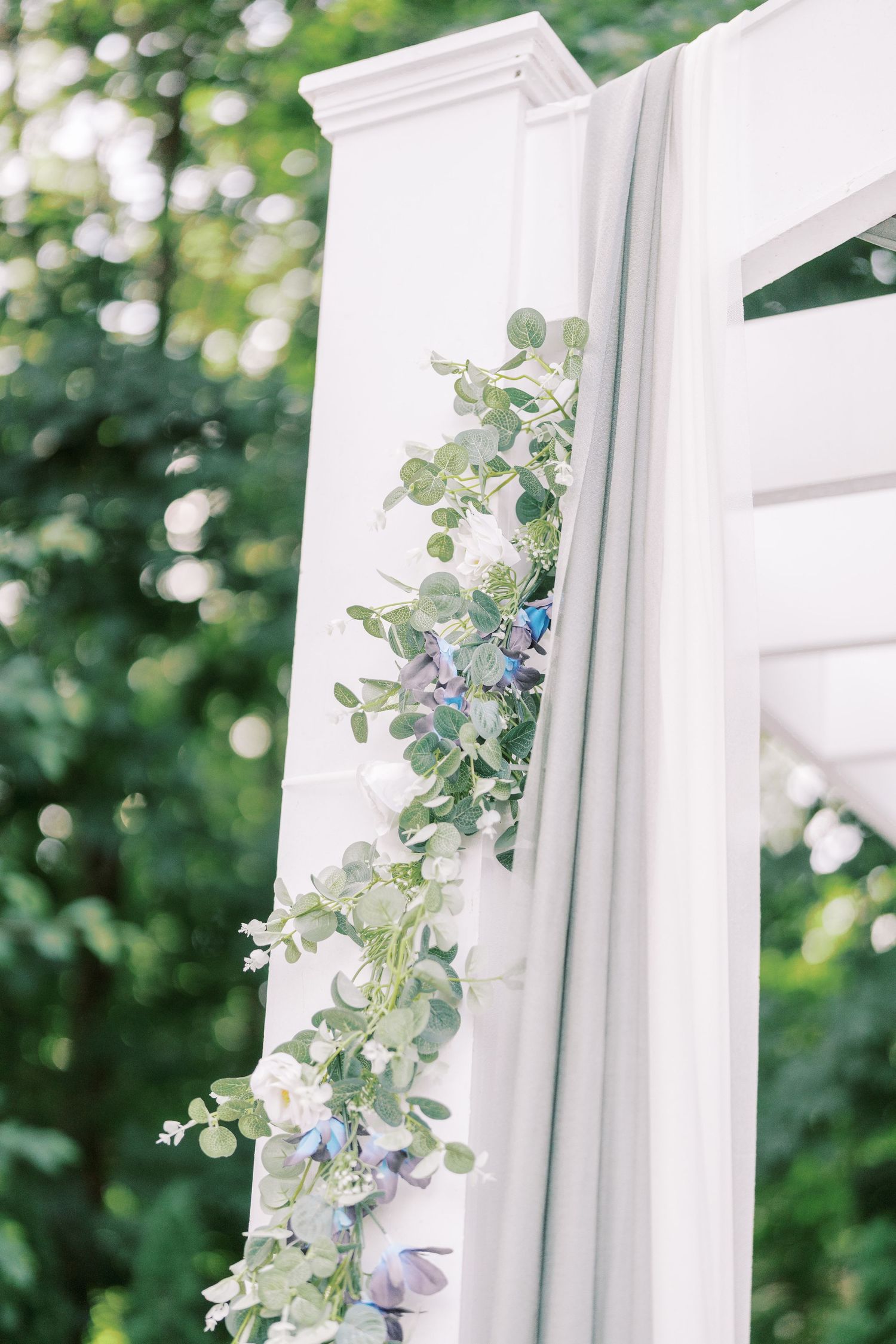 Delicate blue and green eucalyptus garland decorates a white architectural column against a soft bokeh background.