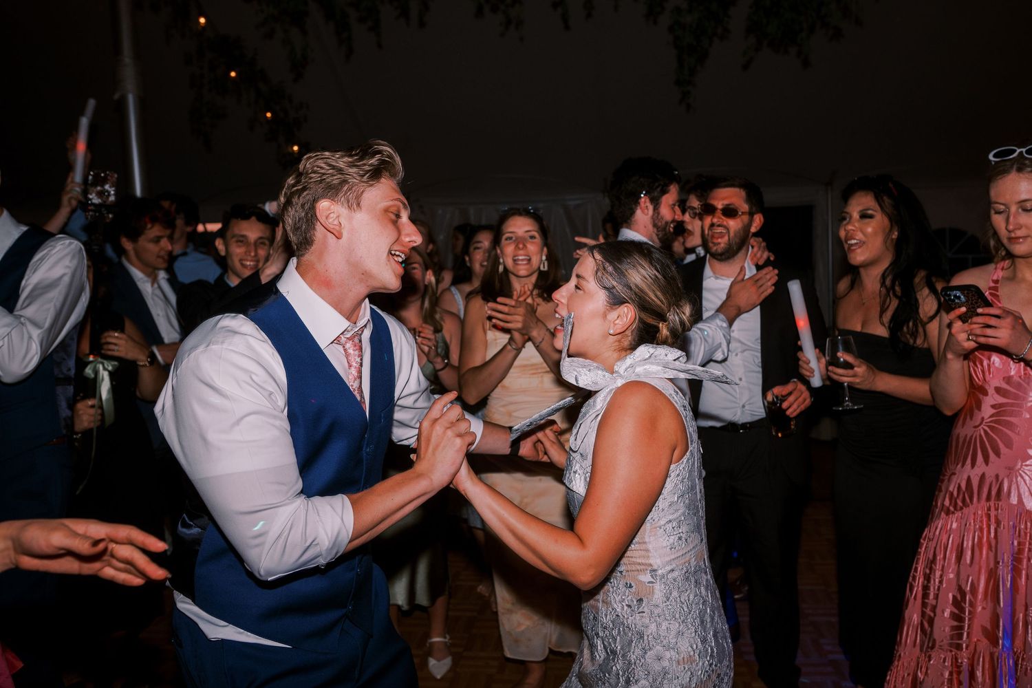 Two wedding guests share an energetic dance moment on the crowded dance floor during an evening reception celebration.