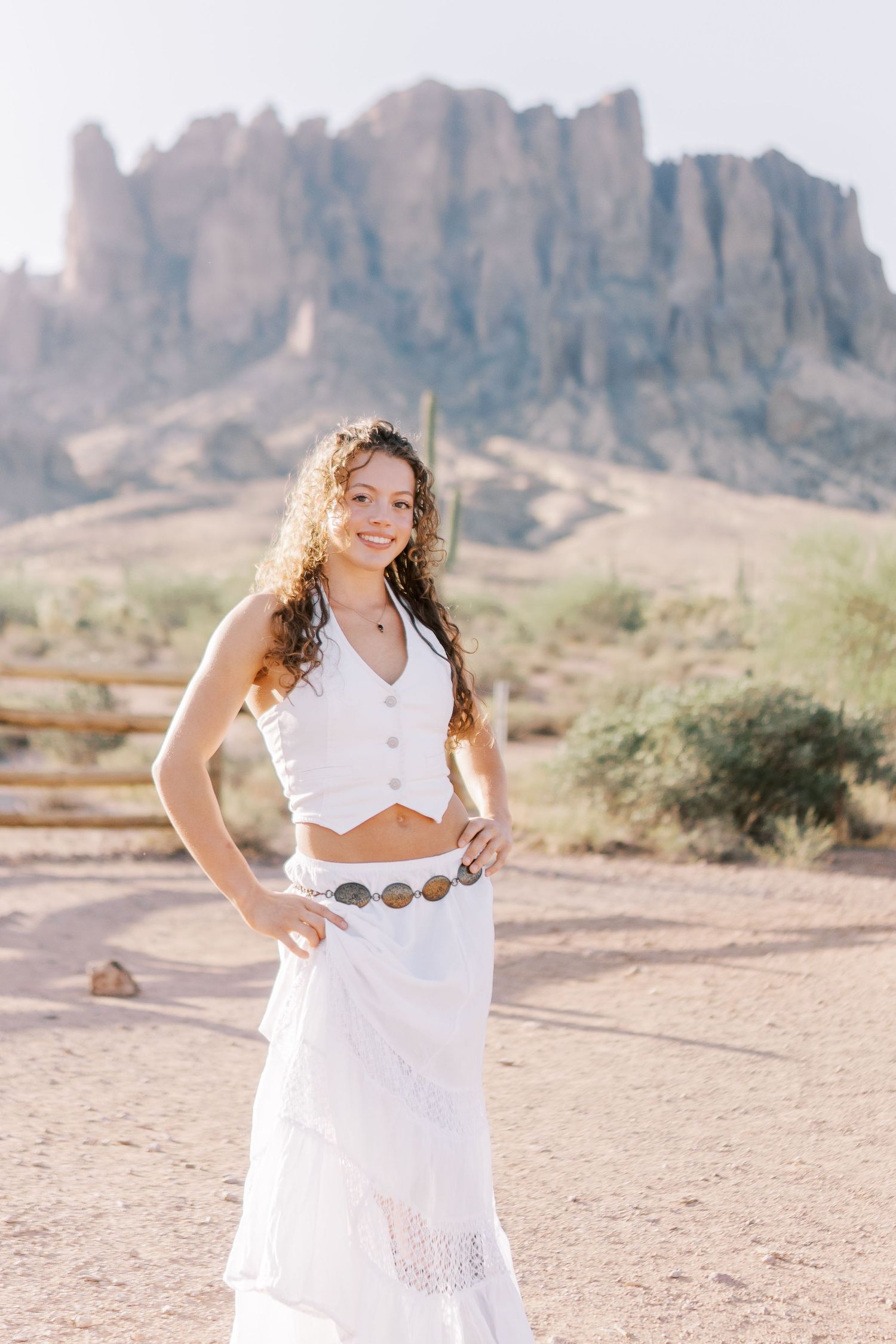Someone in a white bohemian outfit poses against the dramatic backdrop of the Superstition Mountains in Arizona desert.