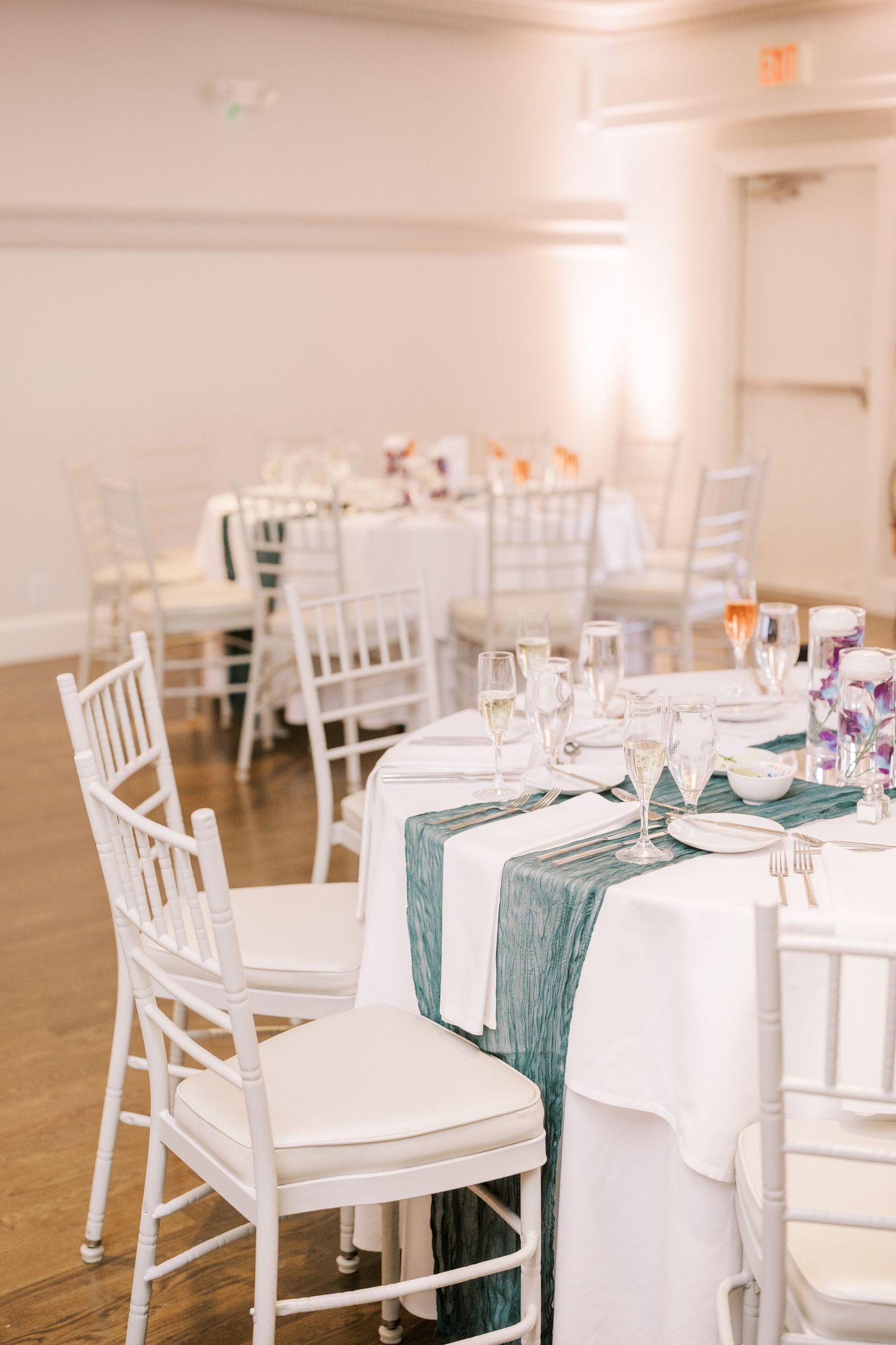 Elegant wedding reception table setting with white chiavari chairs and sage green table runners on crisp white linens.